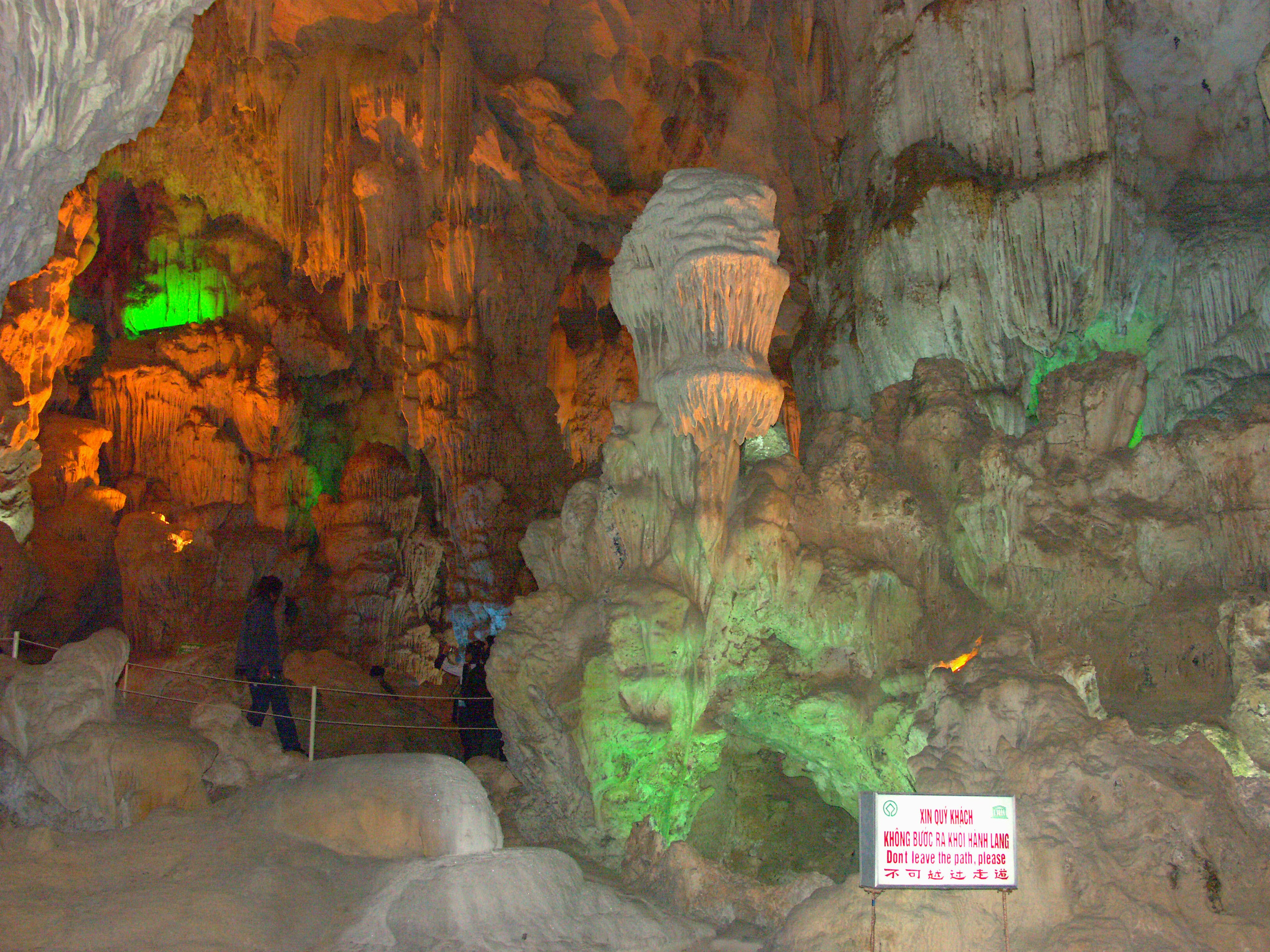 Interno di una grotta illuminato a colori con formazioni di calcare e turisti visibili