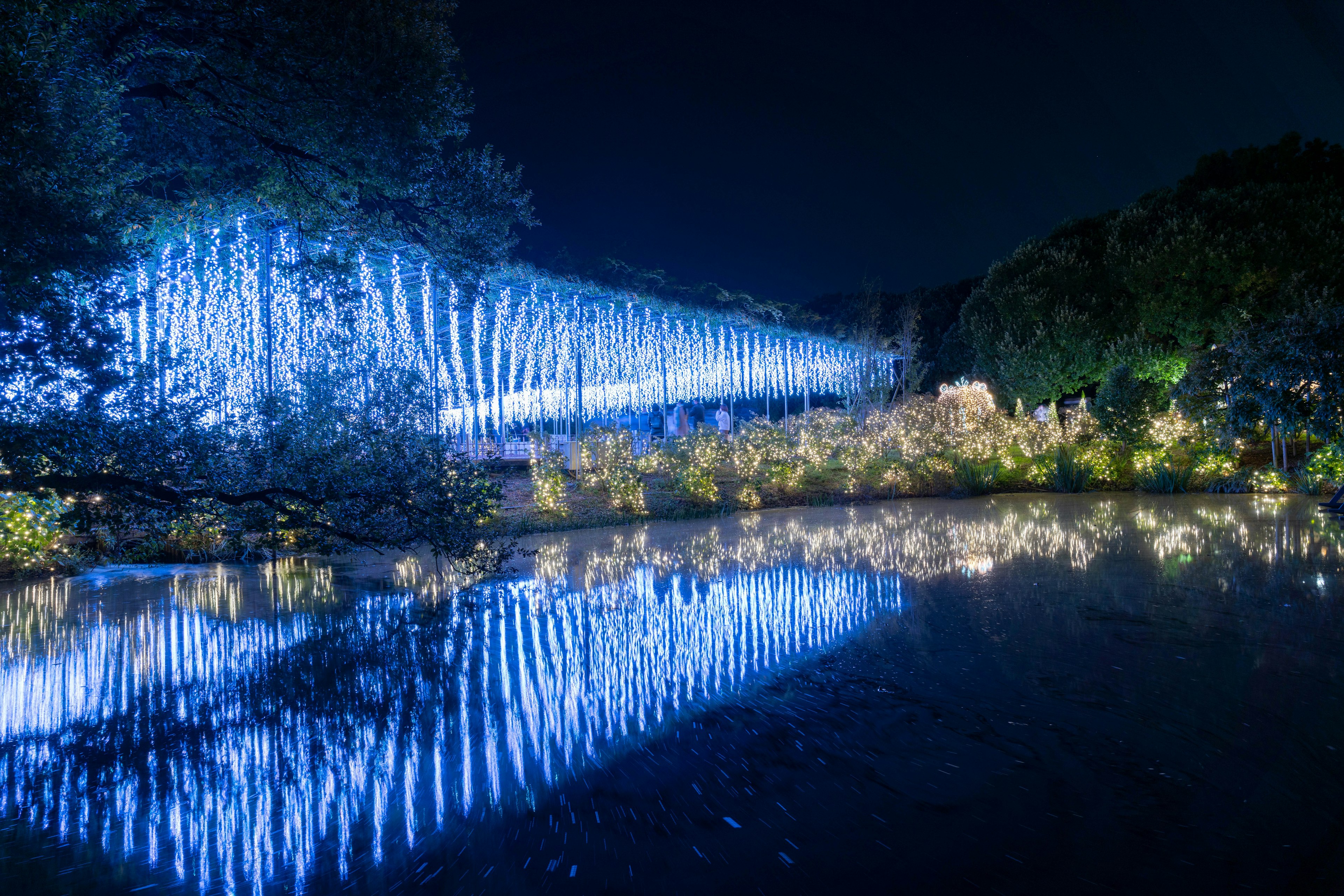 Vista nocturna de una cascada iluminada en azul y su reflejo en el estanque