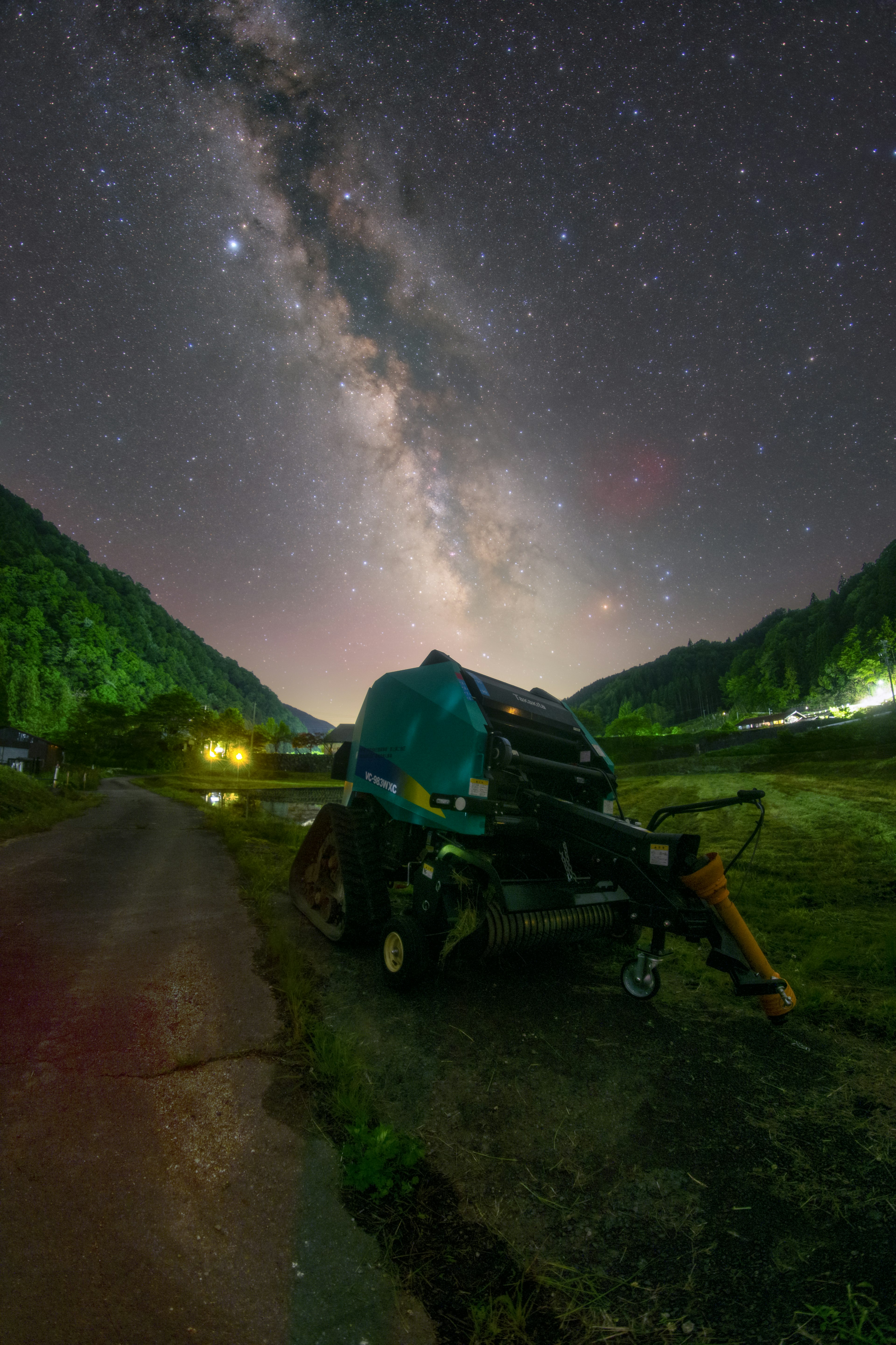 星空の下に停まっている青いトラクターと周囲の山々