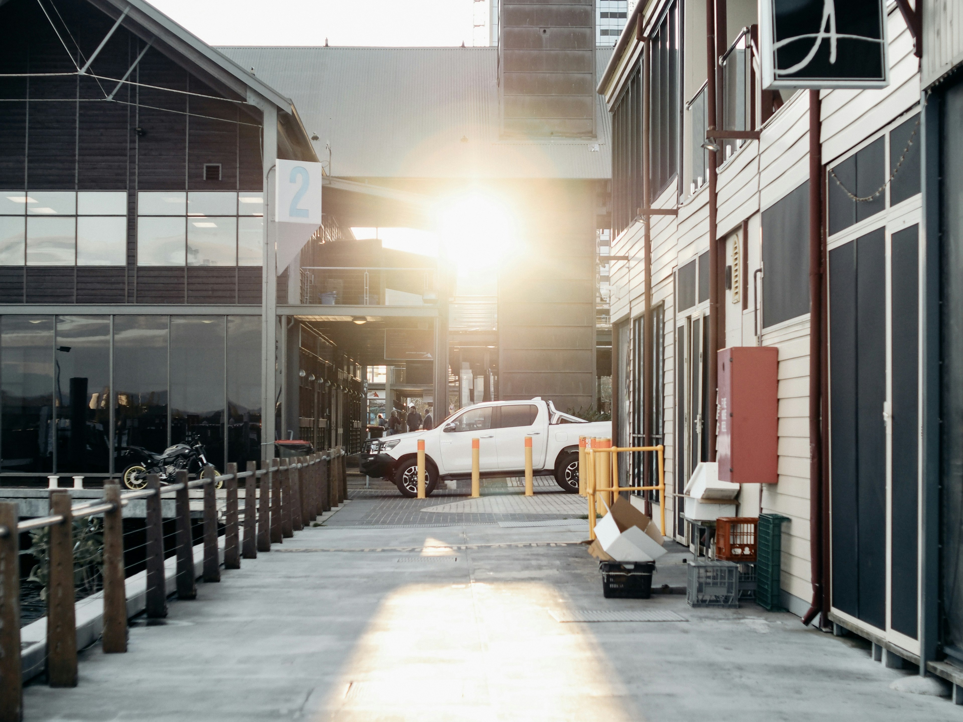 View of a waterfront walkway with buildings and a car, sunlight shining through