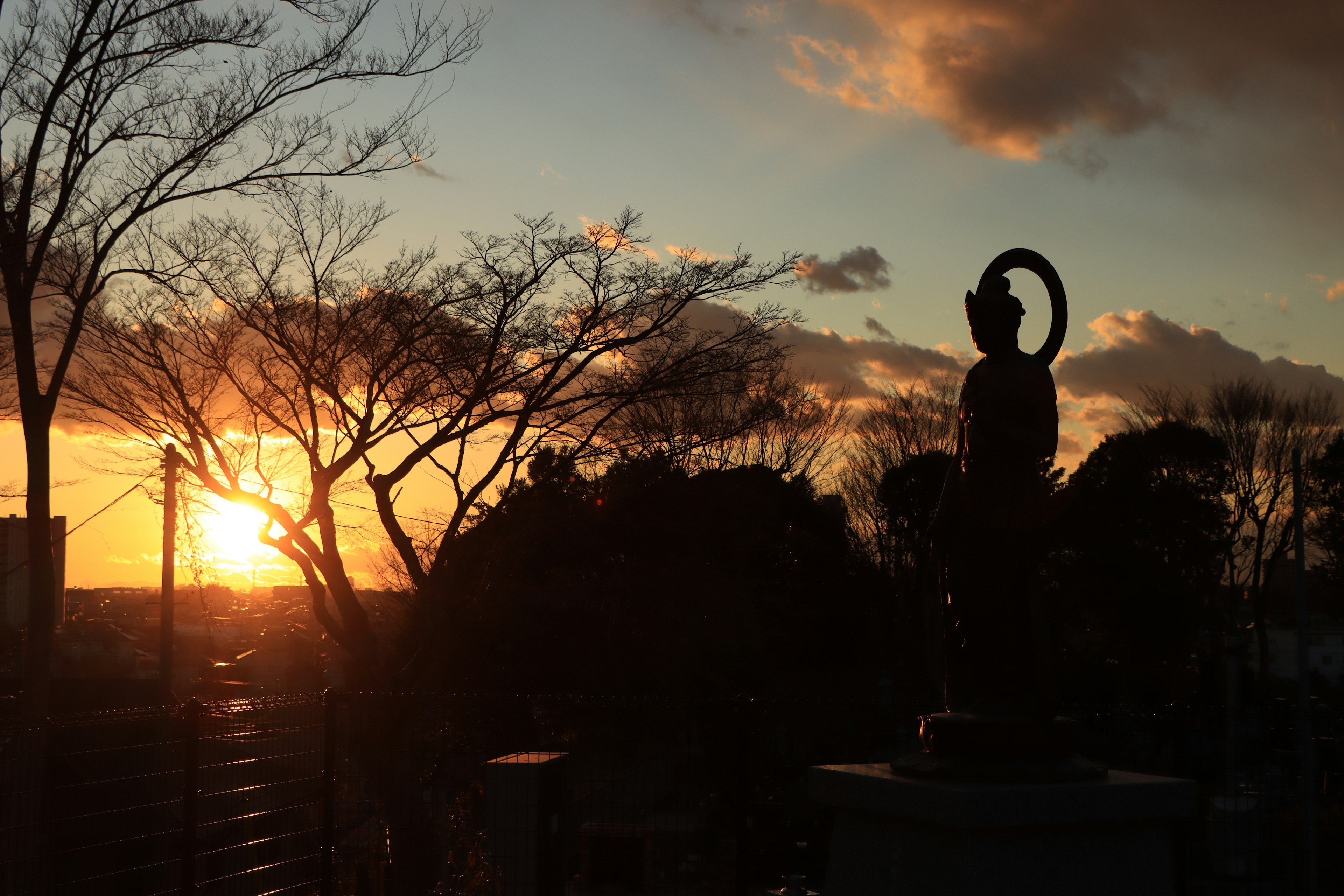 Silhouette einer Statue und Bäume gegen einen Sonnenuntergang