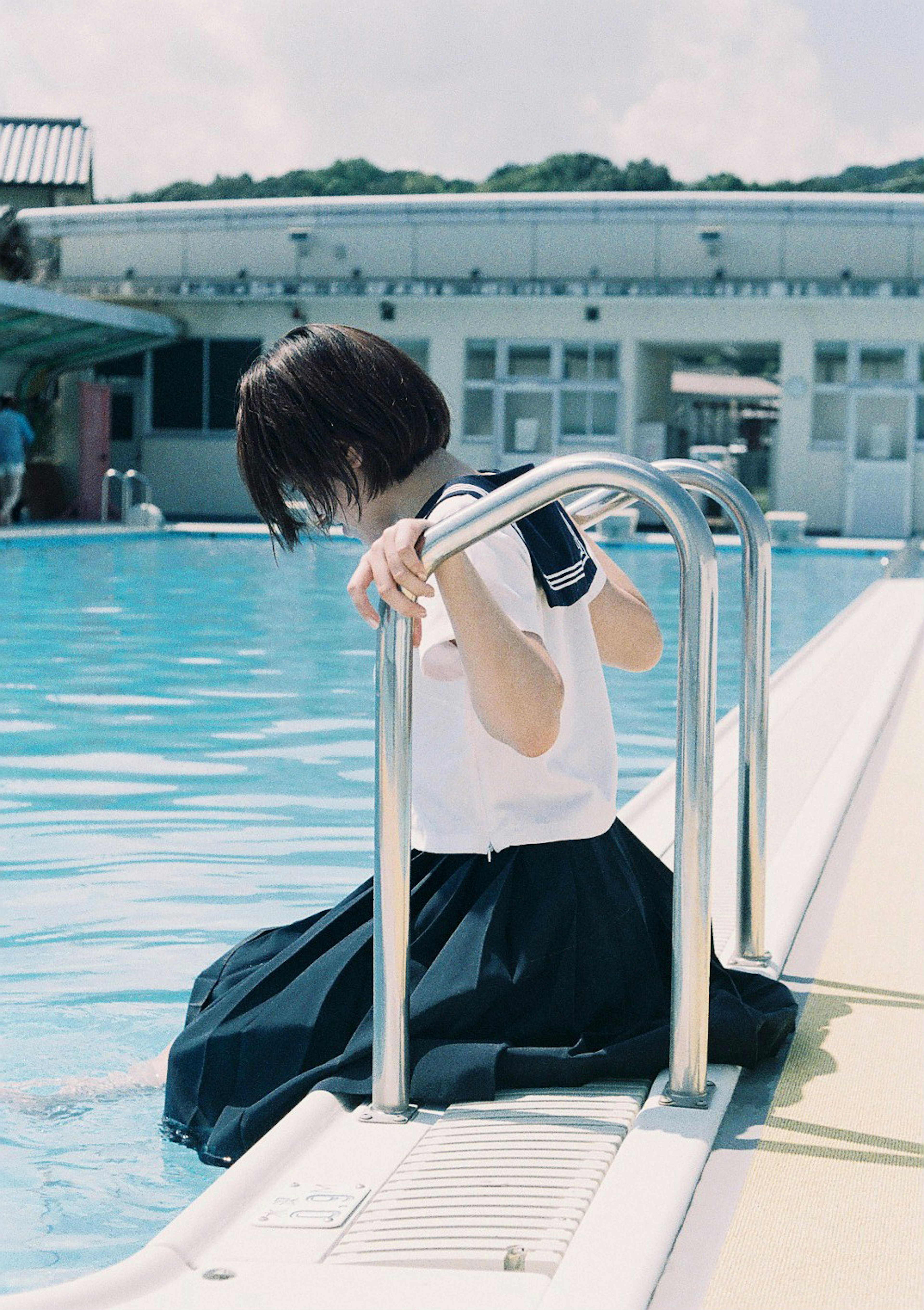 Chica en uniforme escolar sumergiendo los pies en una piscina