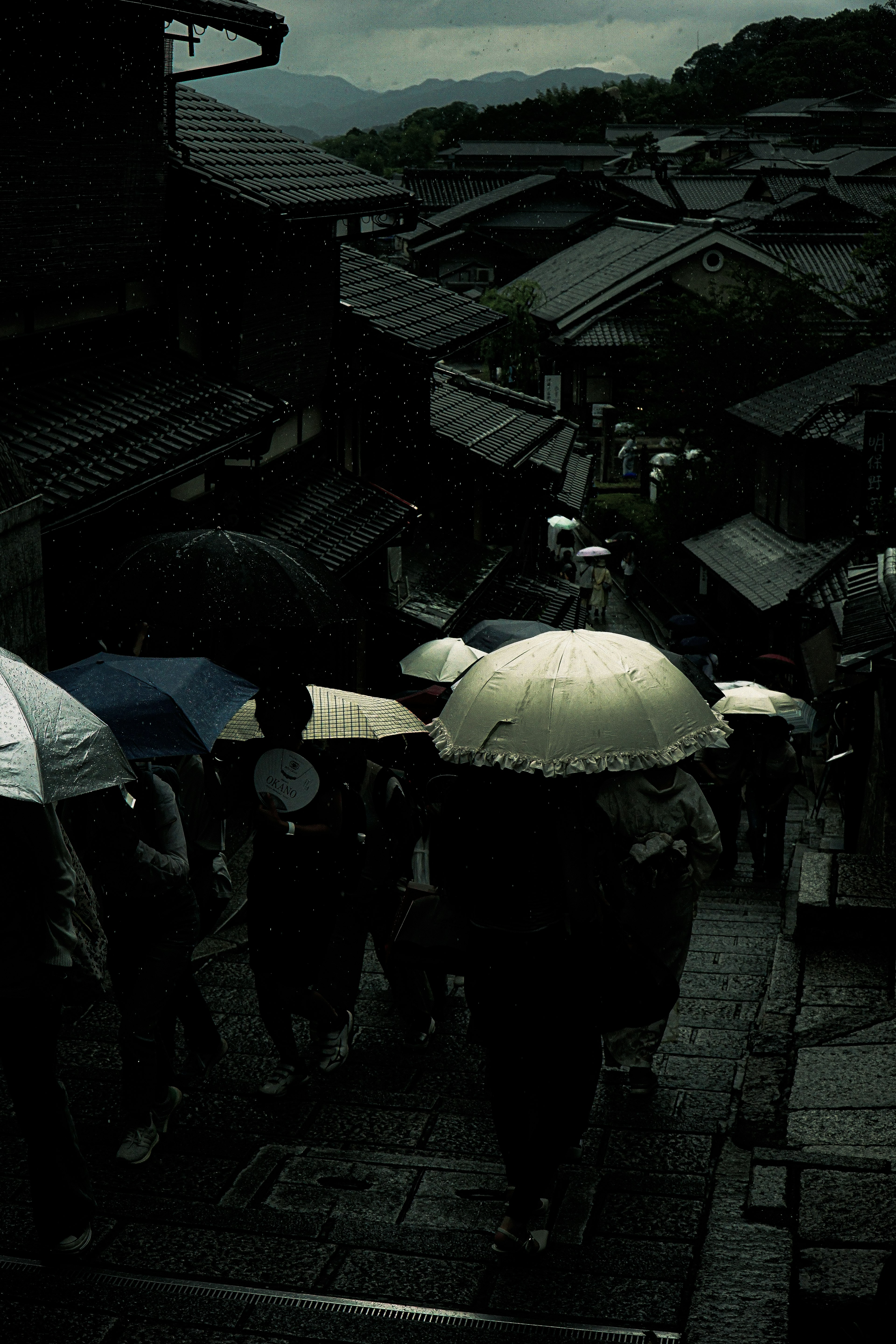 People with umbrellas walking down stairs in a dark, atmospheric street scene