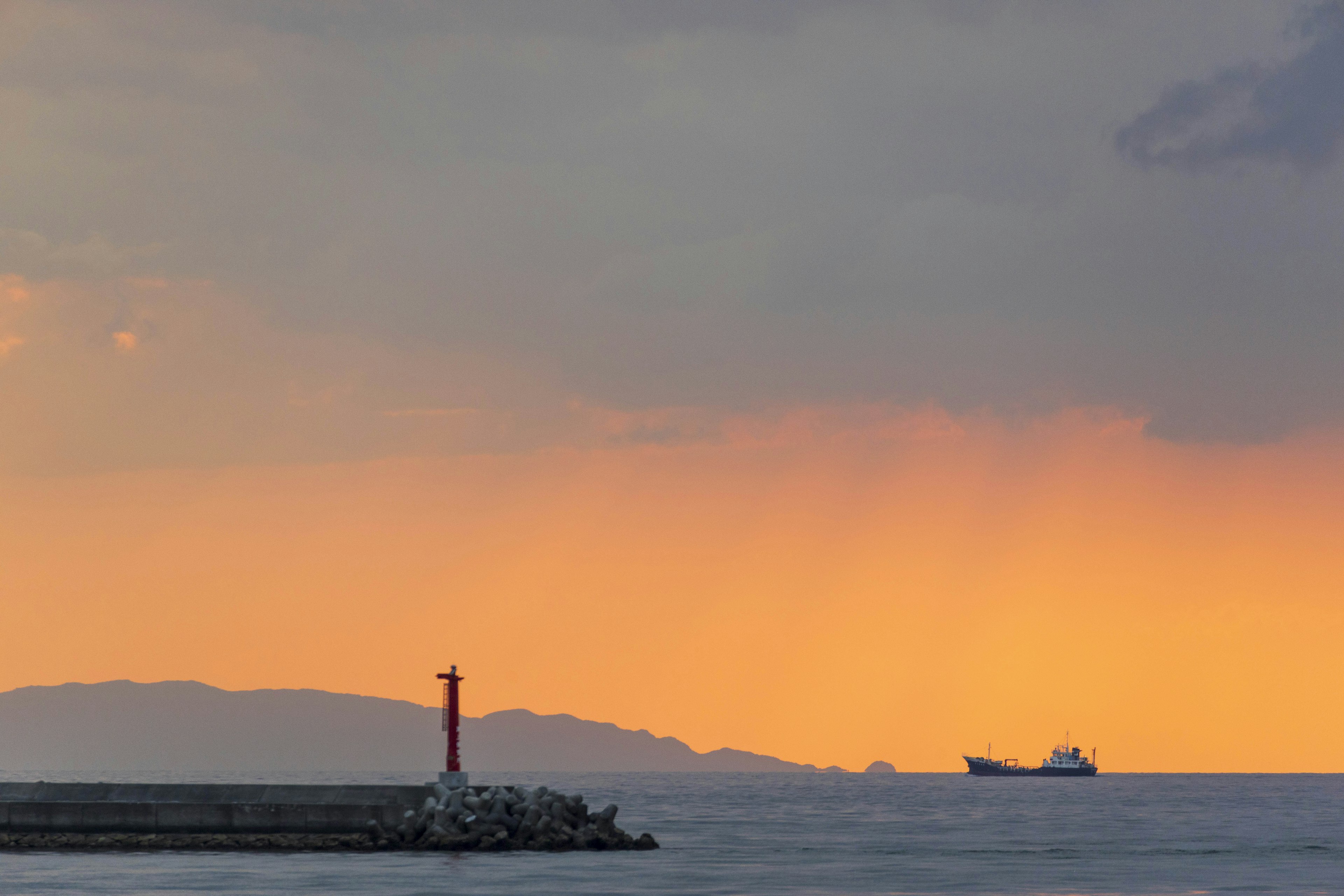 Leuchtturm steht im Meer bei Sonnenuntergang mit einem entfernten Schiff