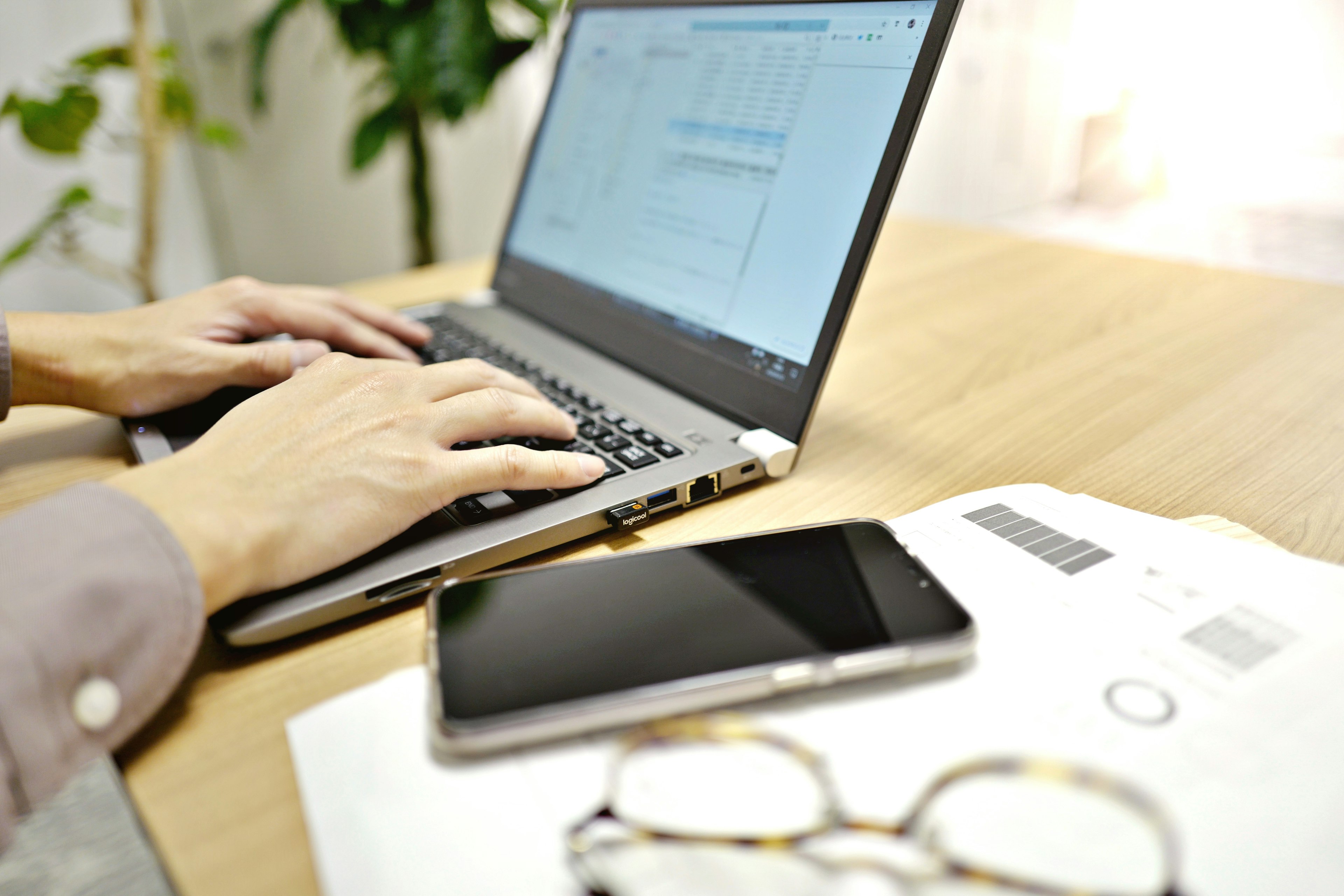 Manos escribiendo en una laptop con un teléfono inteligente y documentos en un escritorio