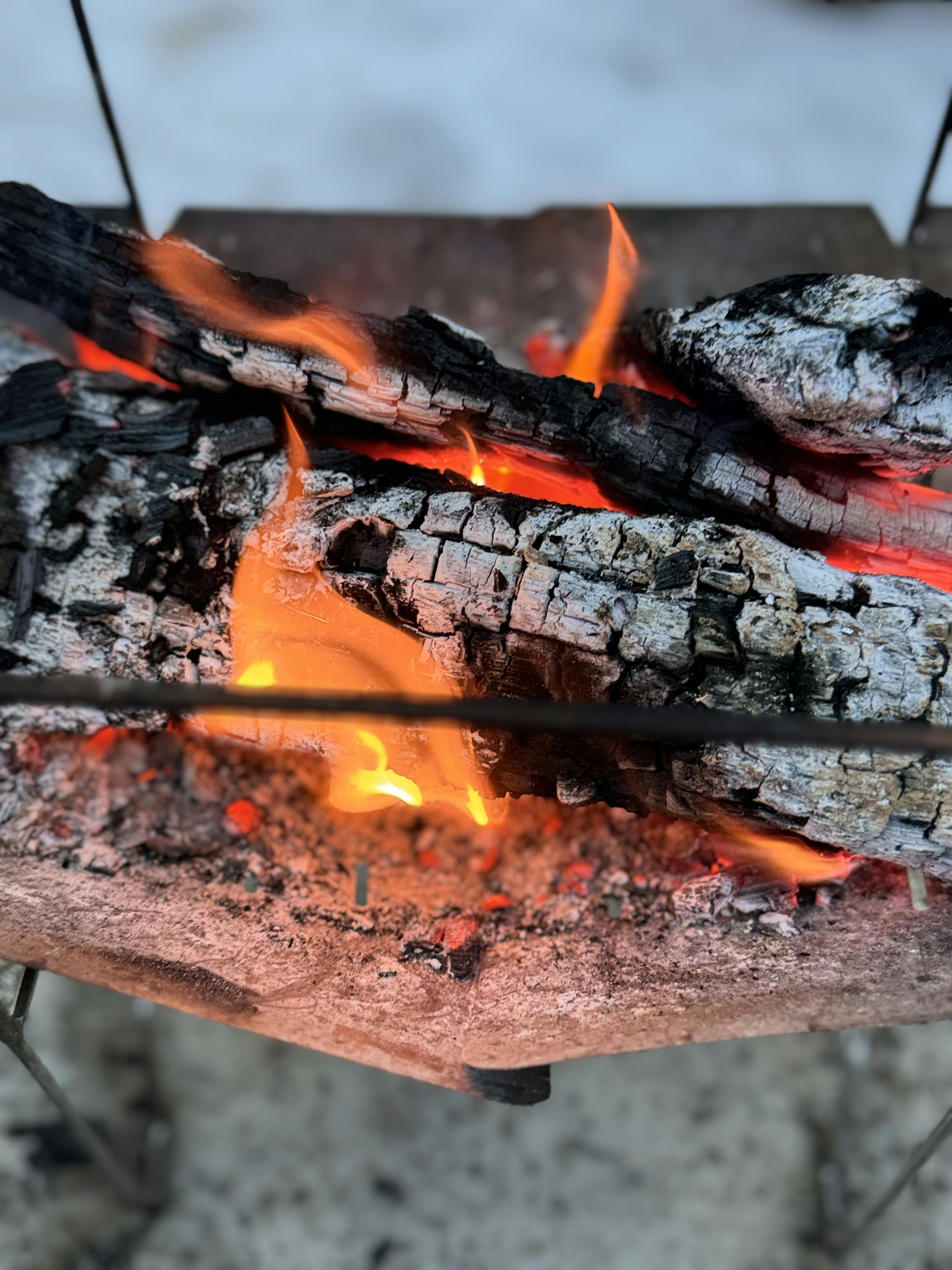 Brennende Holzstücke mit orangefarbenen Flammen und grauer Asche