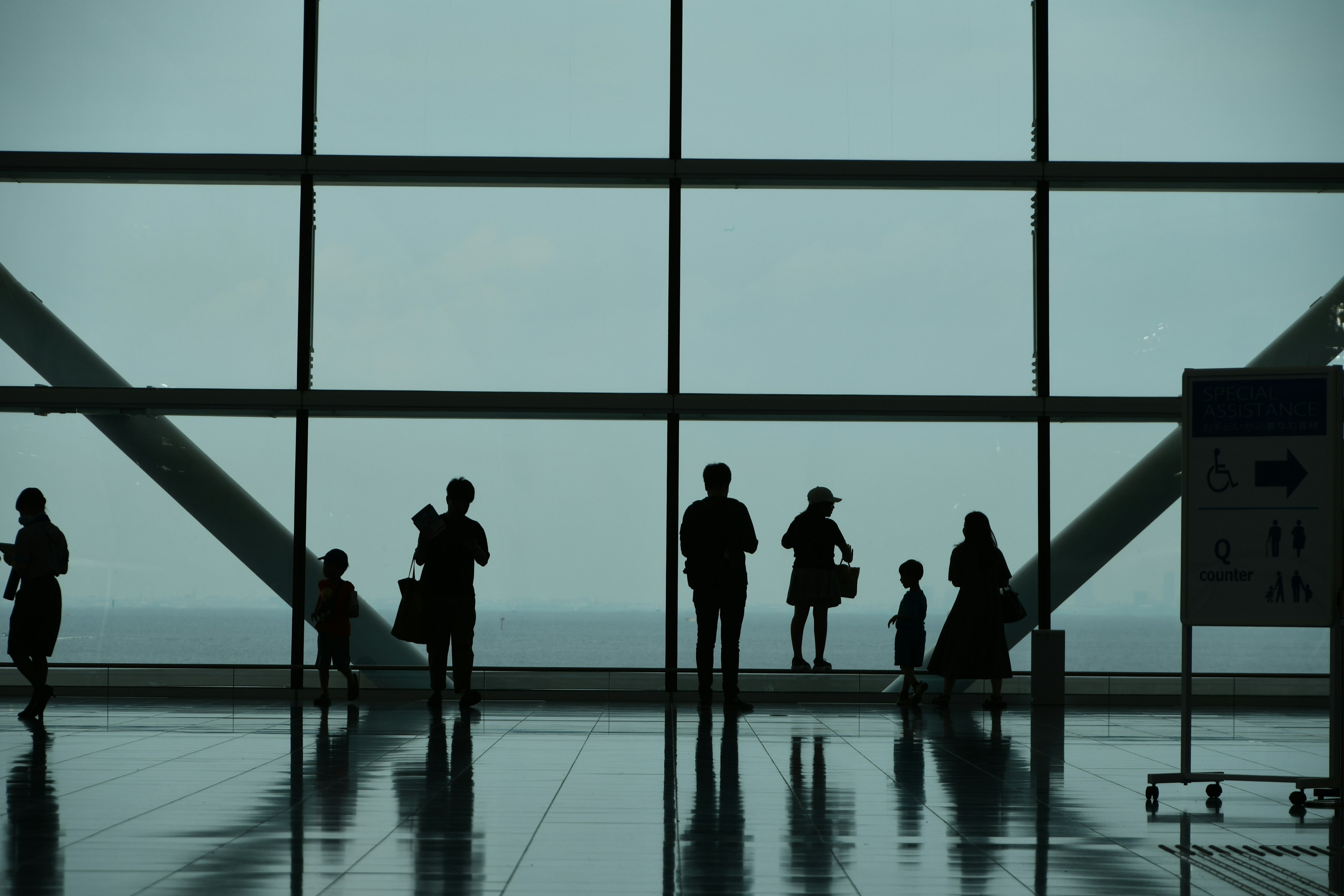 Siluetas de personas en una ventana del aeropuerto con vista al mar