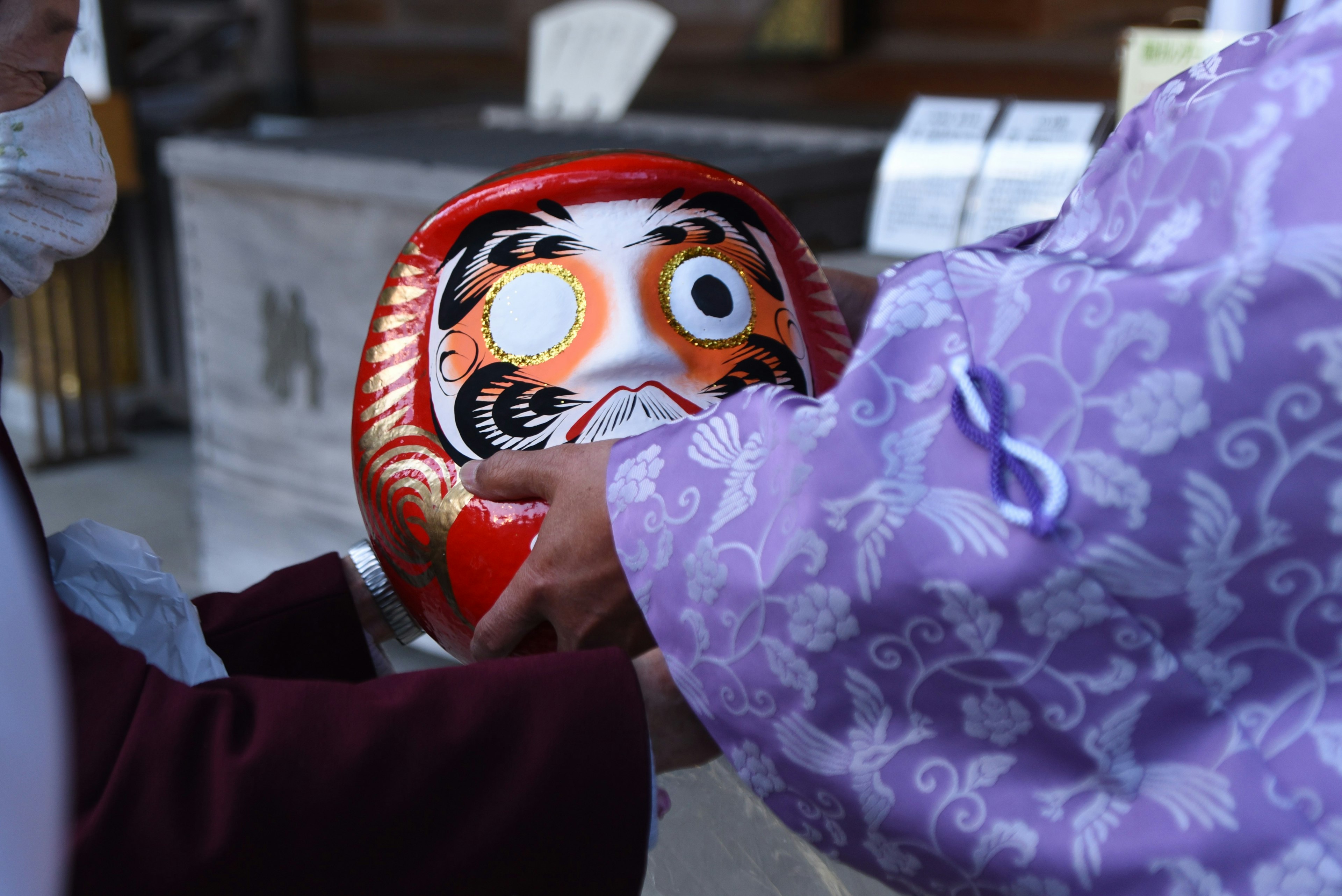 Manos intercambiando una muñeca Daruma roja con una prenda morada