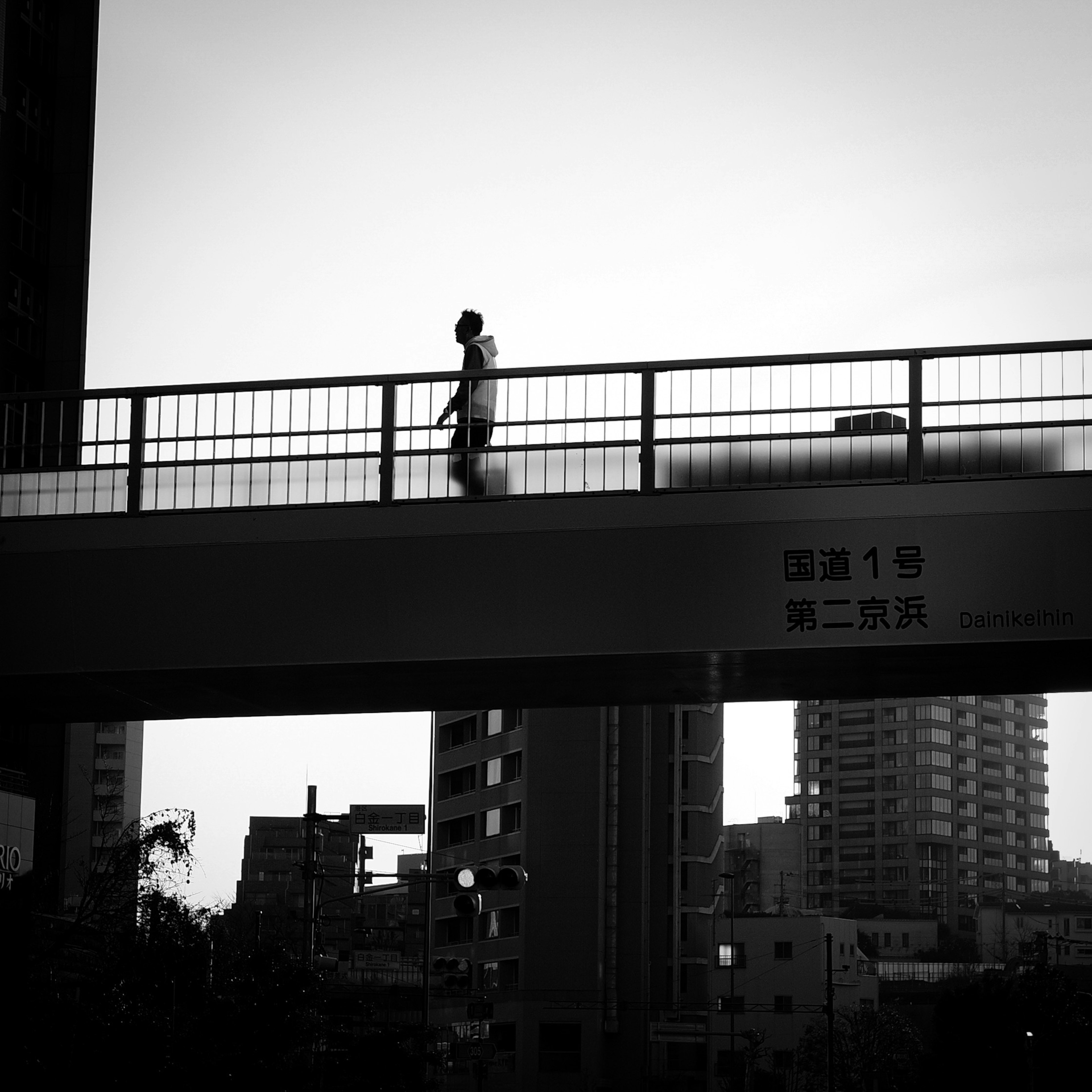 Paisaje urbano en blanco y negro con una persona caminando sobre un puente y edificios circundantes