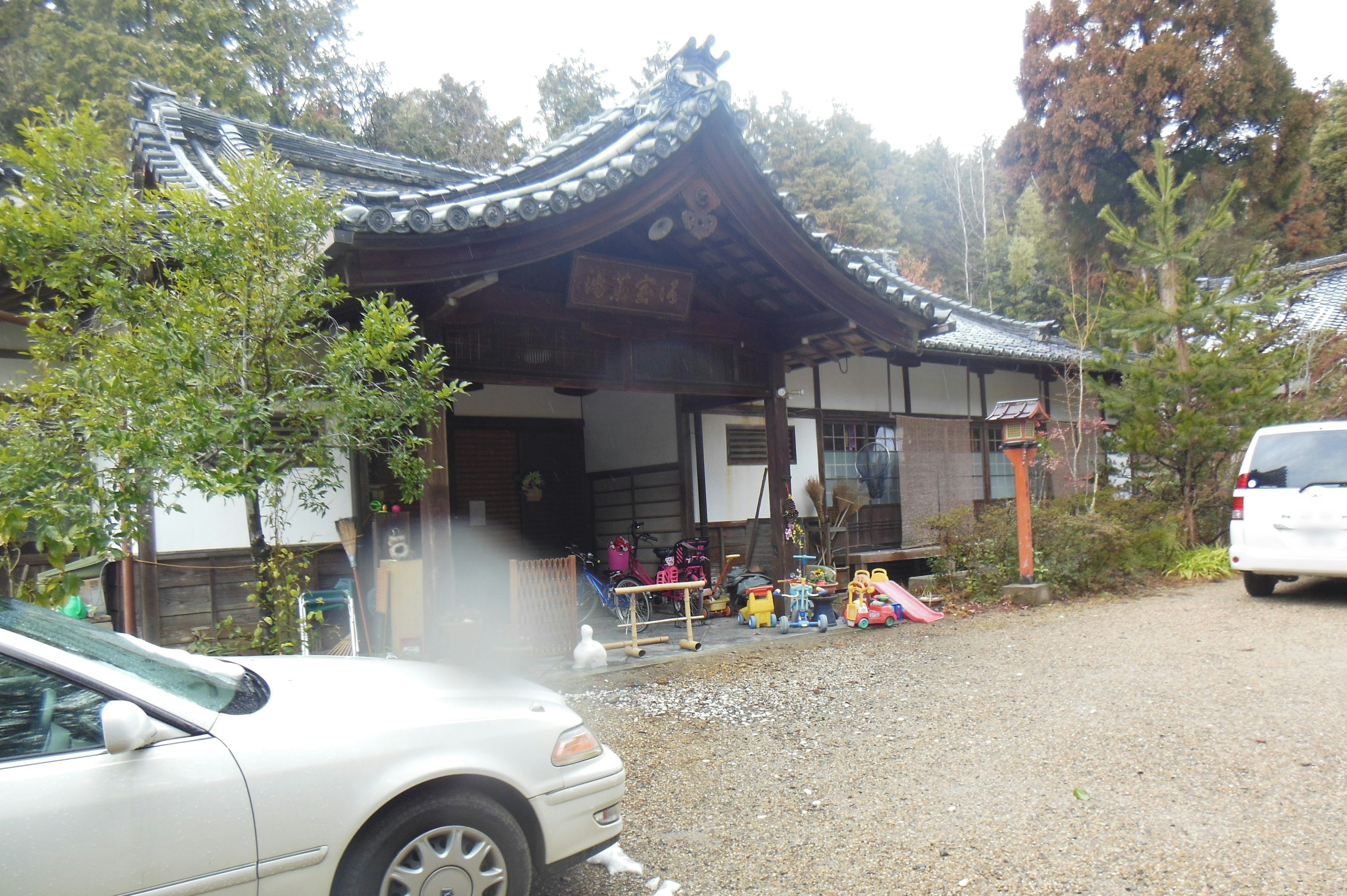 Bild eines traditionellen japanischen Hauses mit einem markanten Dach geparktes Auto in einem Garten, der mit Kinderspielzeug übersät ist