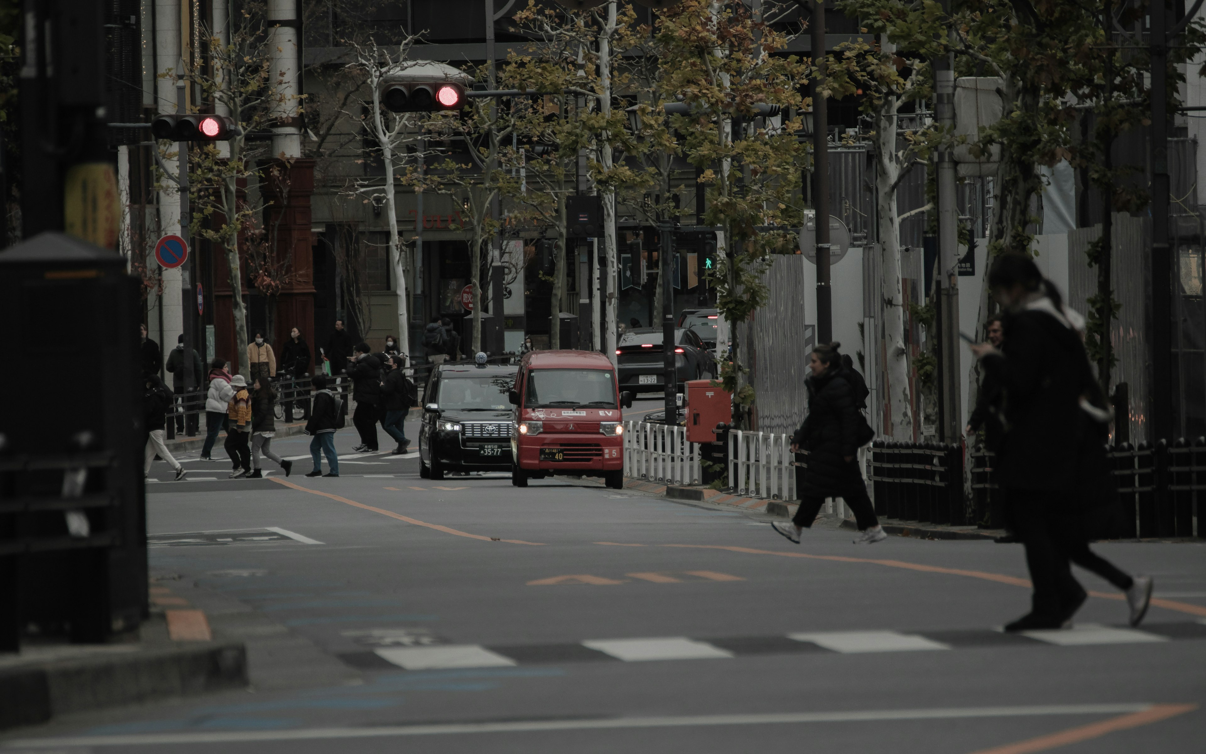 薄暗い街角で信号待ちの人々と赤い車が映る