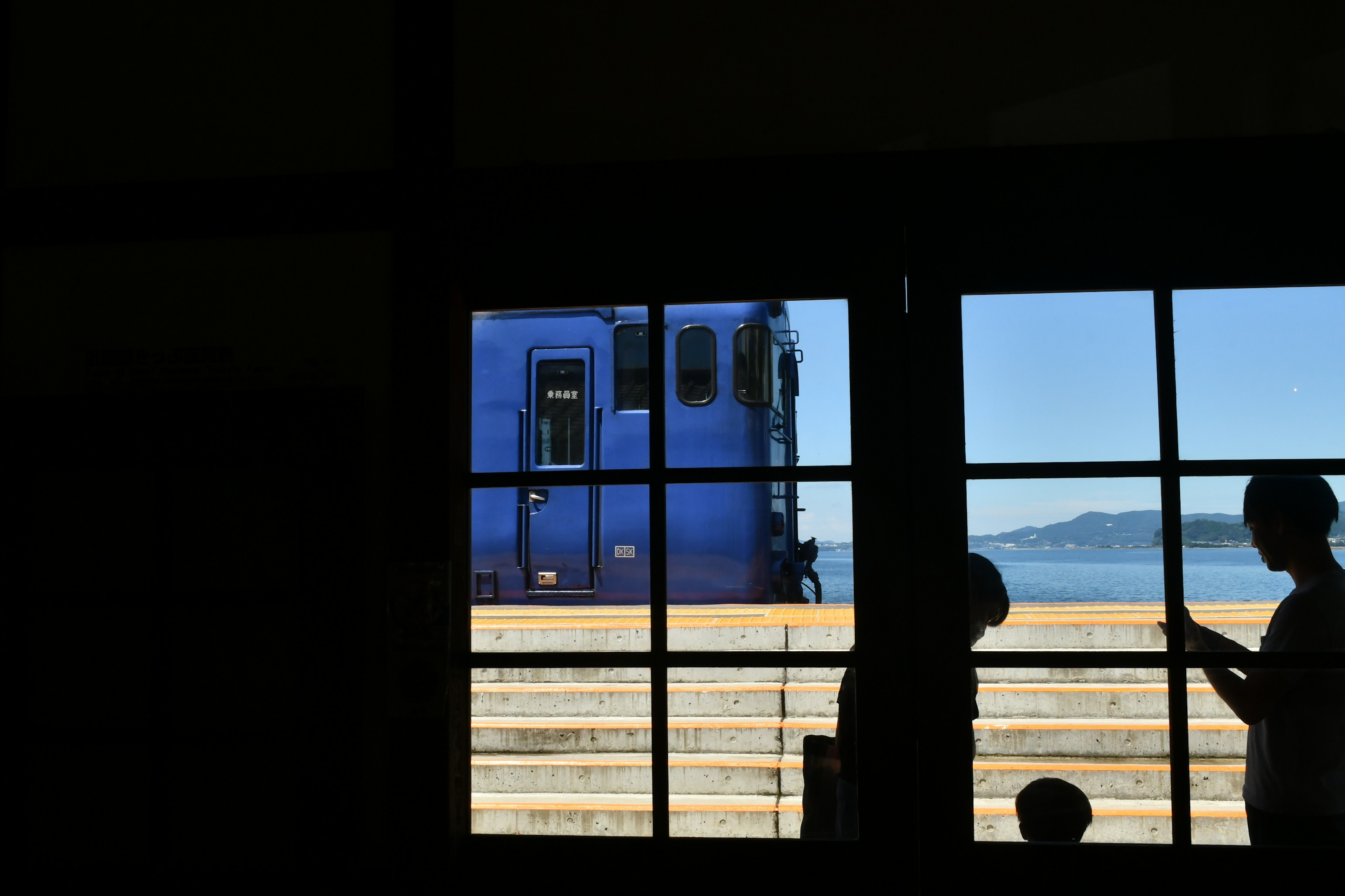 Silhouettes de personnes avec un train bleu visible à travers une fenêtre