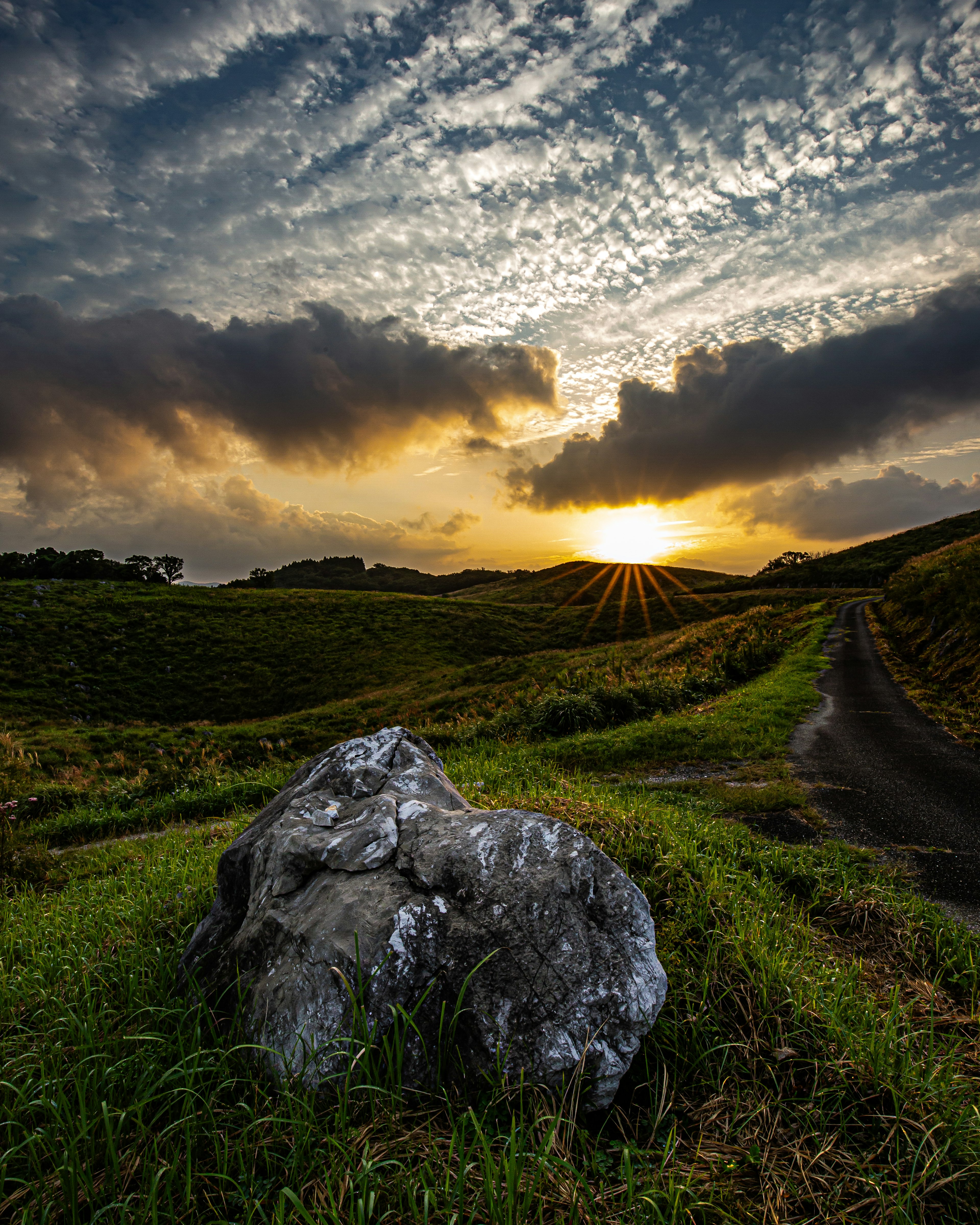 一块大岩石在风景如画的乡村景观中，背景是美丽的日落和云彩