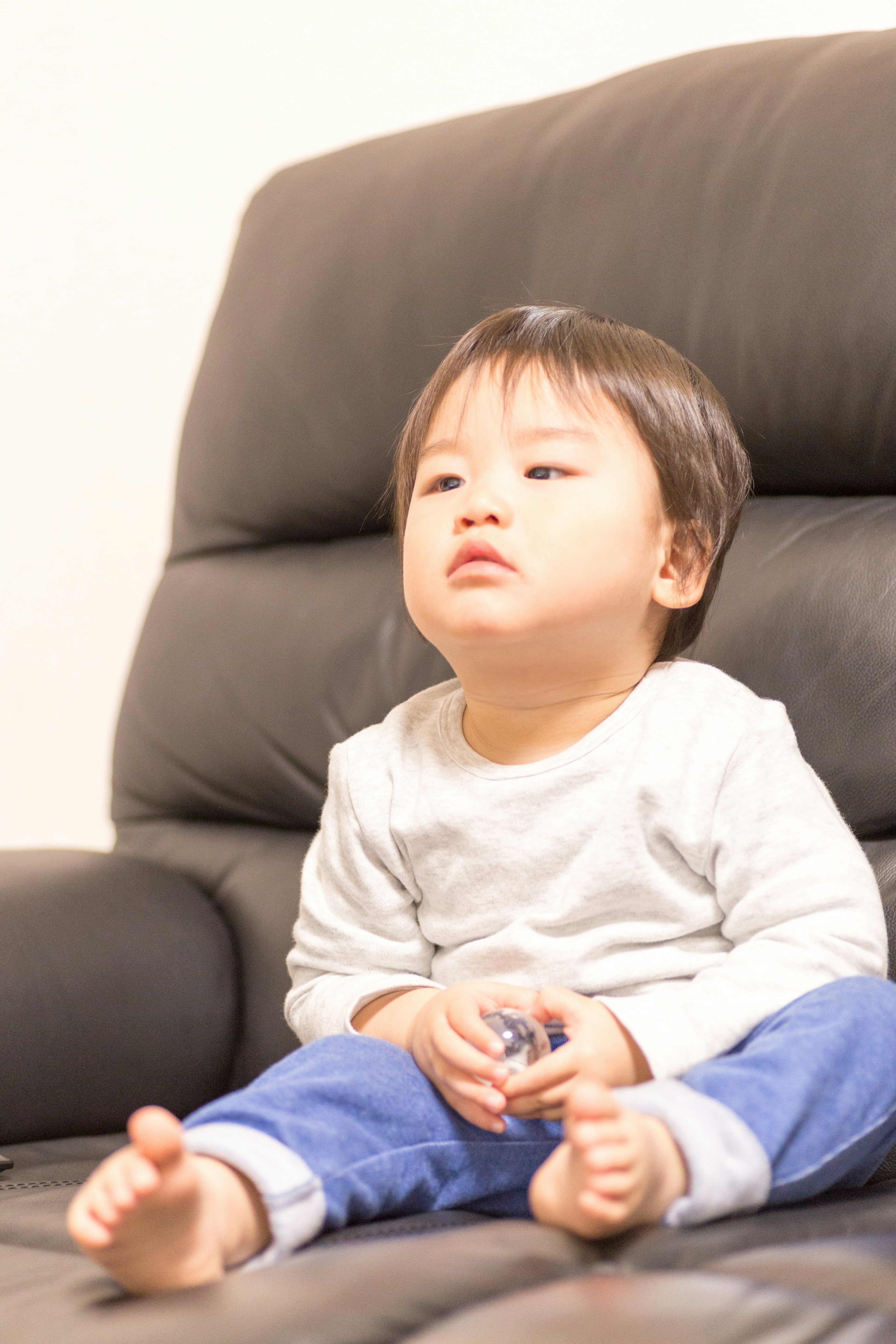 A young child sitting on a black sofa with a pensive expression