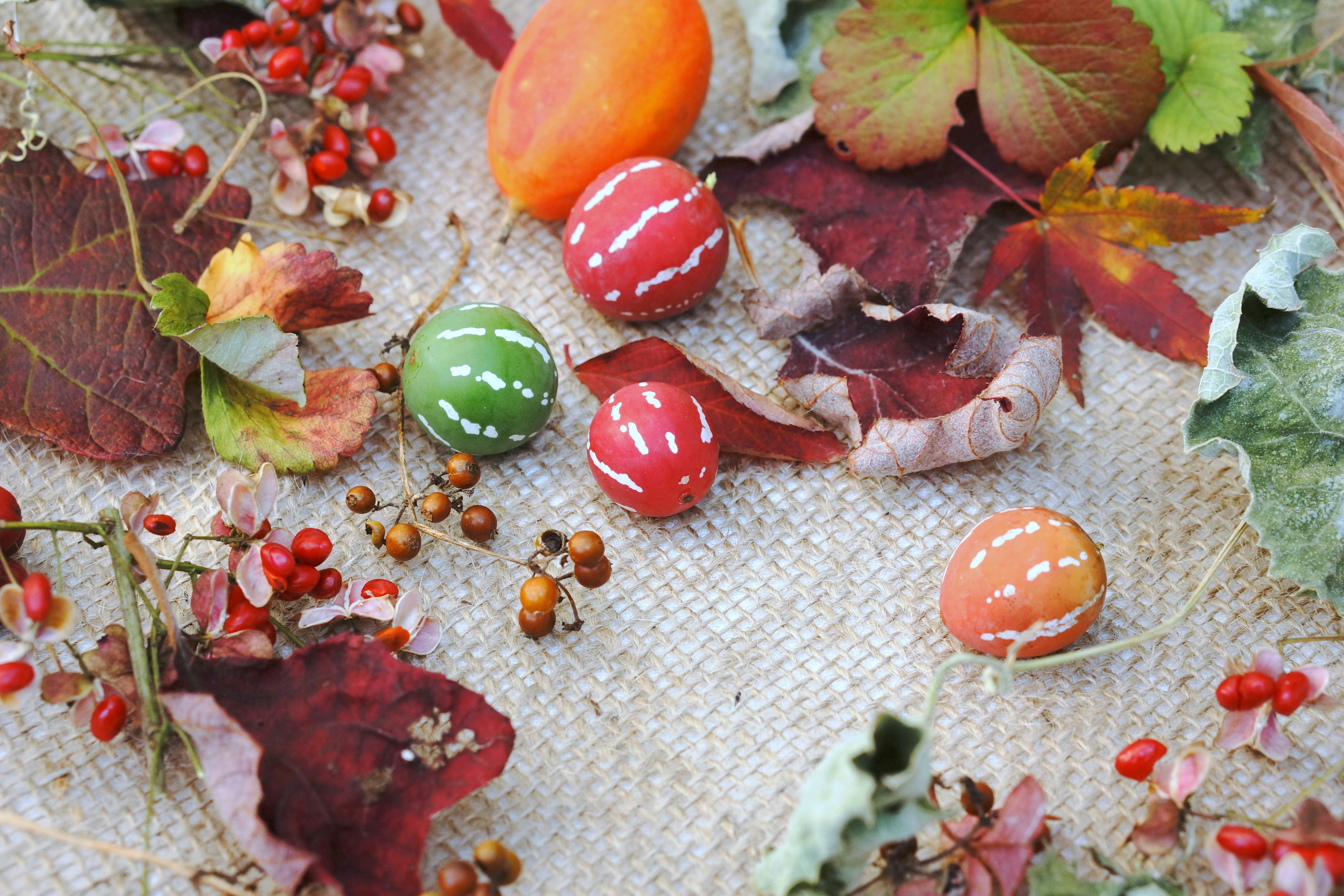 A scene featuring autumn leaves and decorated small orange and green balls scattered on a surface