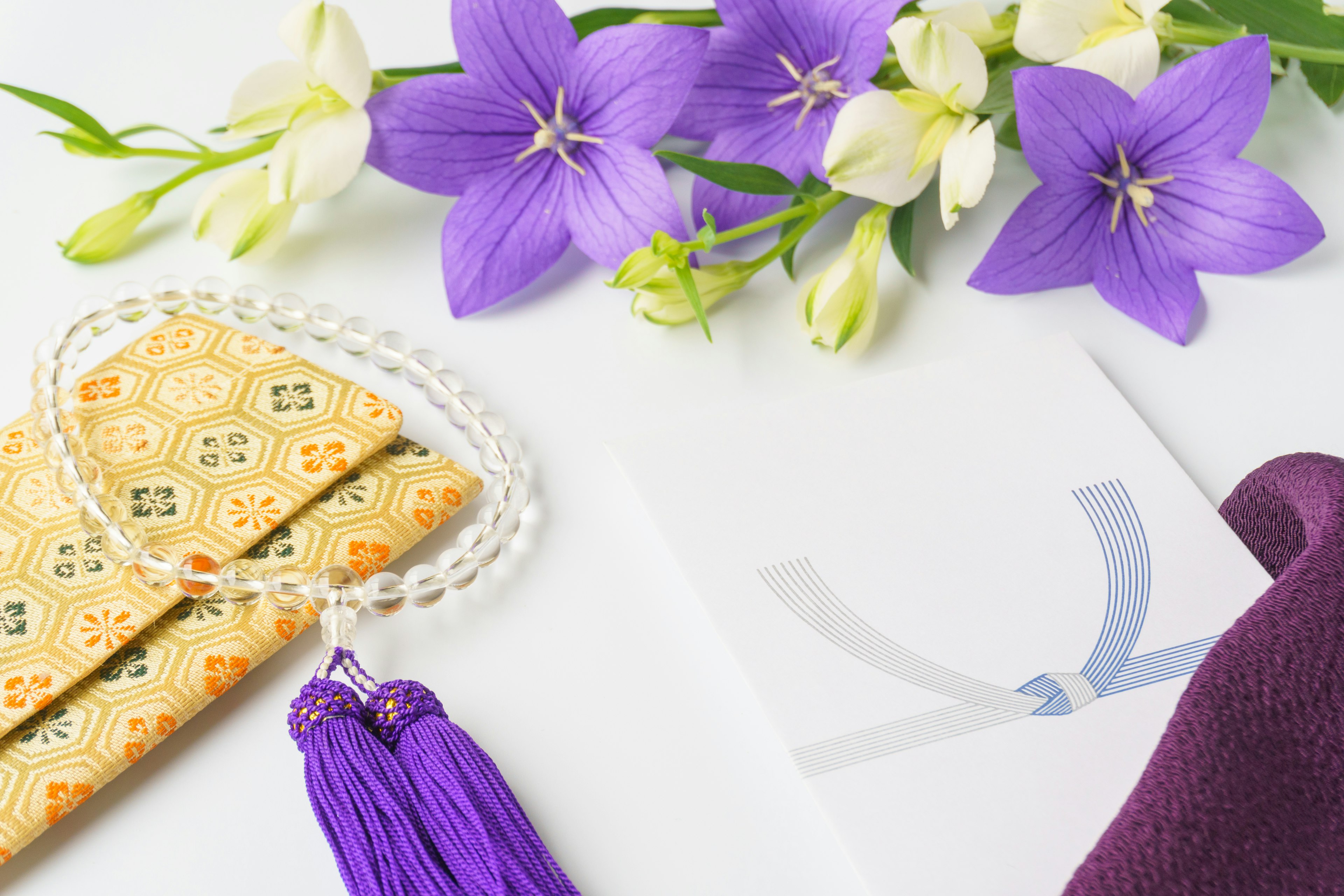 Arreglo de flores moradas y blancas con un collar de perlas y un sobre decorativo