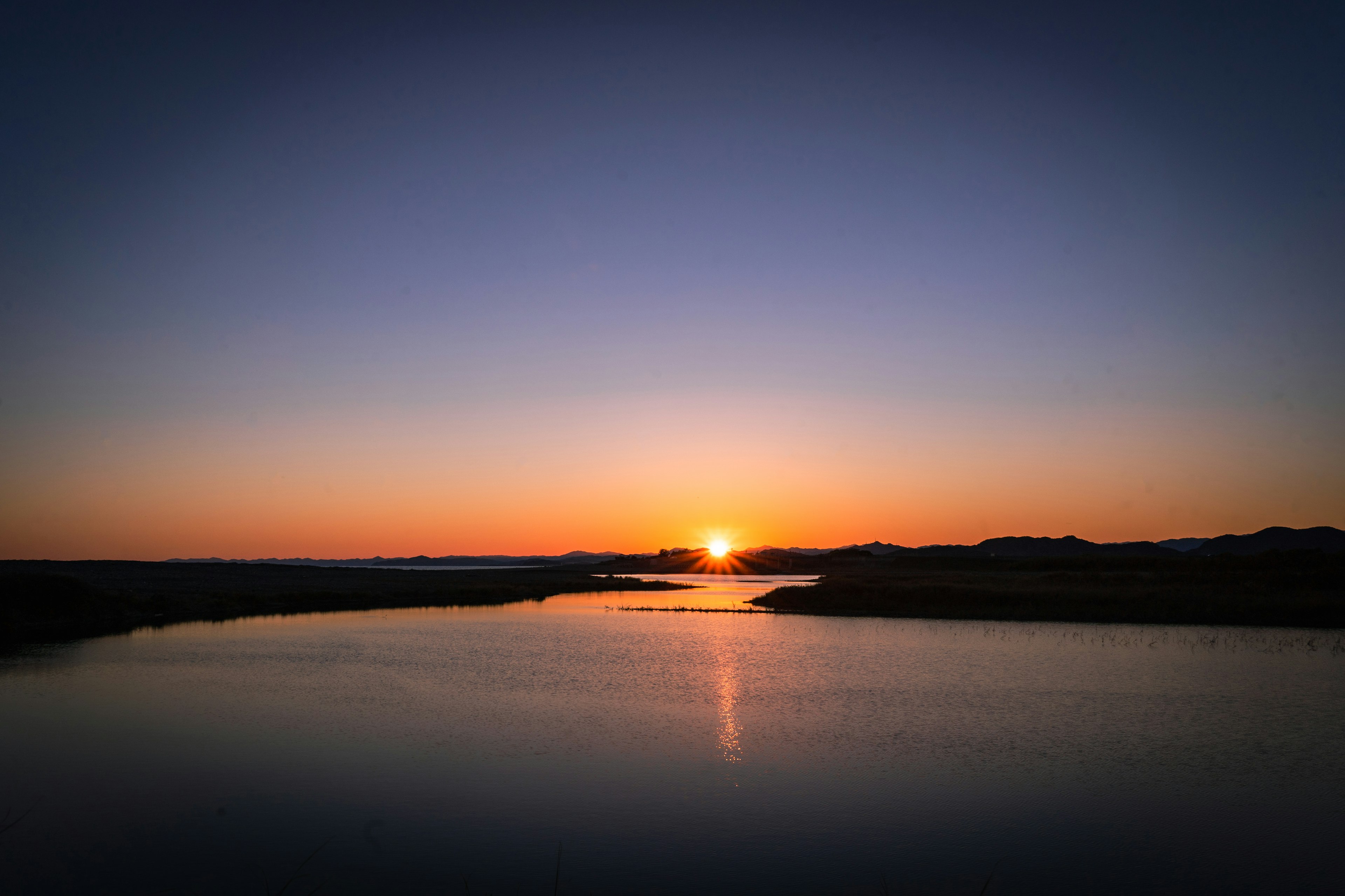 静かな川のほとりに沈む夕日とその反射