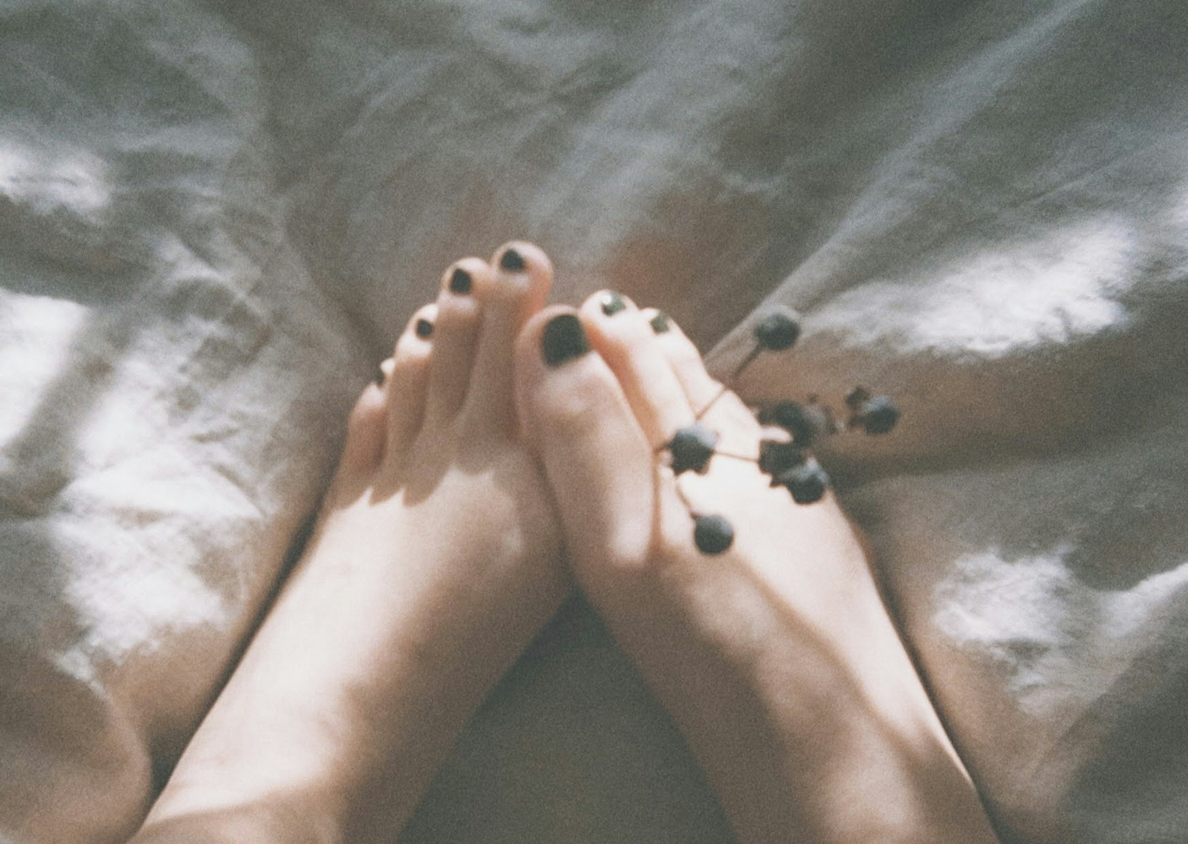 Photo de pieds avec vernis à ongles foncé et petites baies placées entre eux sur un tissu doux