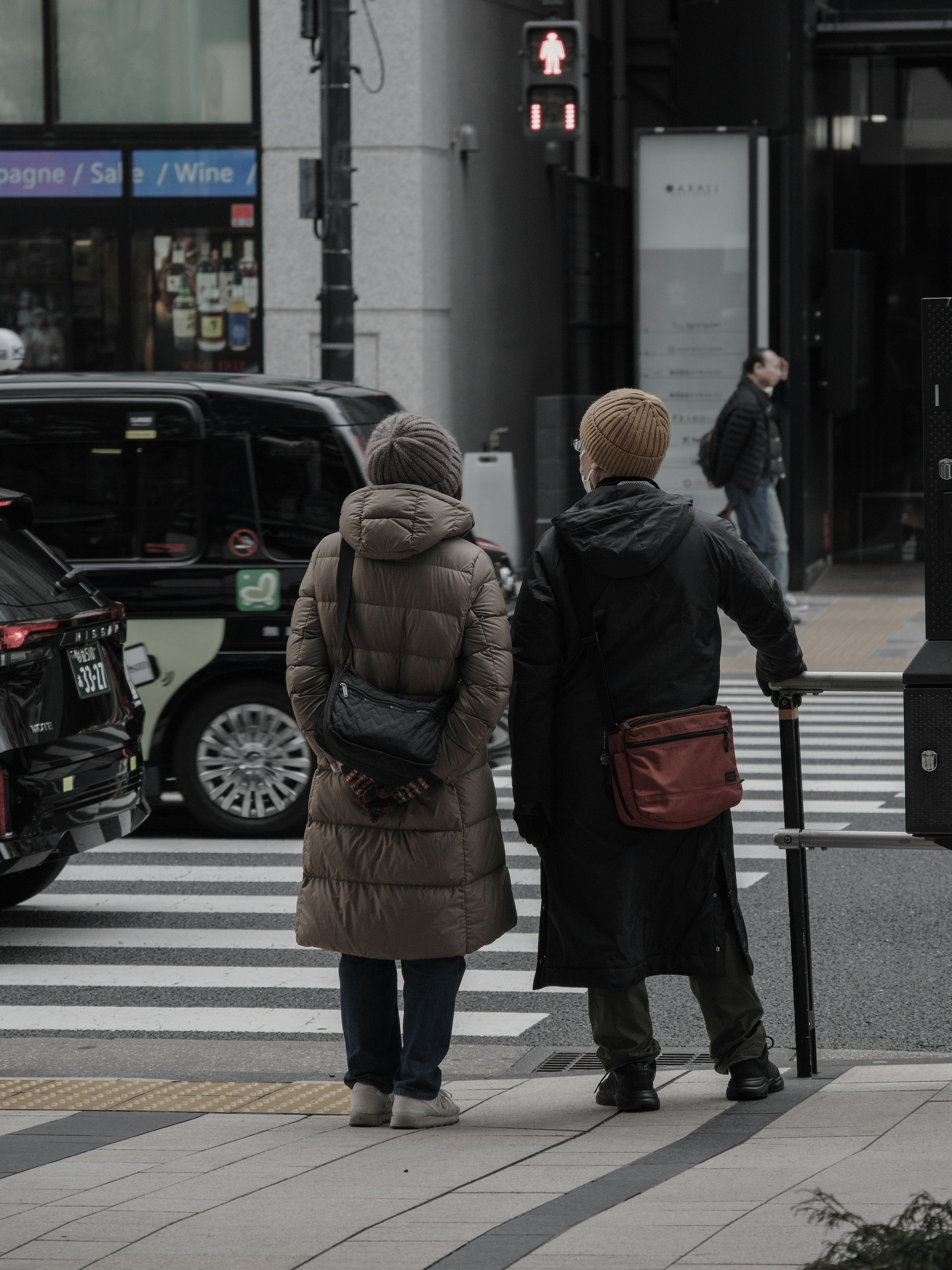 Two individuals waiting at a crosswalk one holding a cane