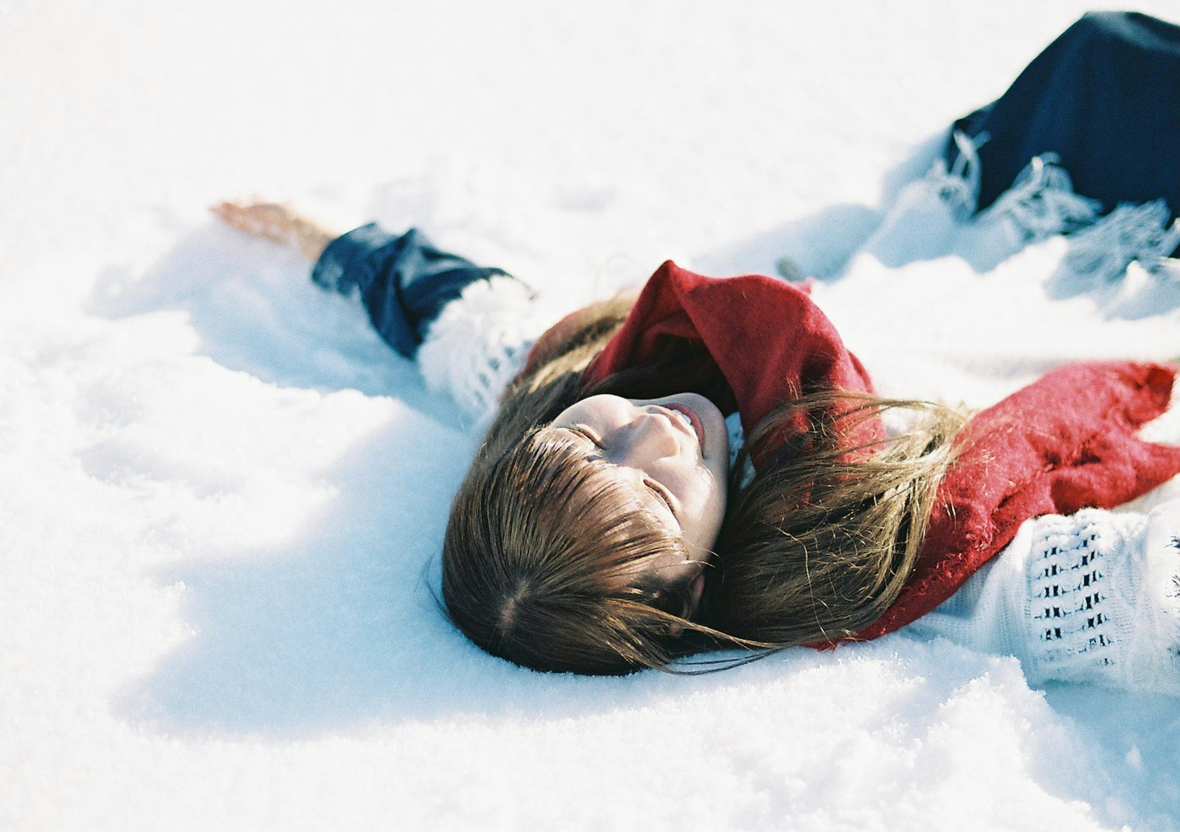 Donna distesa nella neve con una sciarpa rossa e un maglione bianco