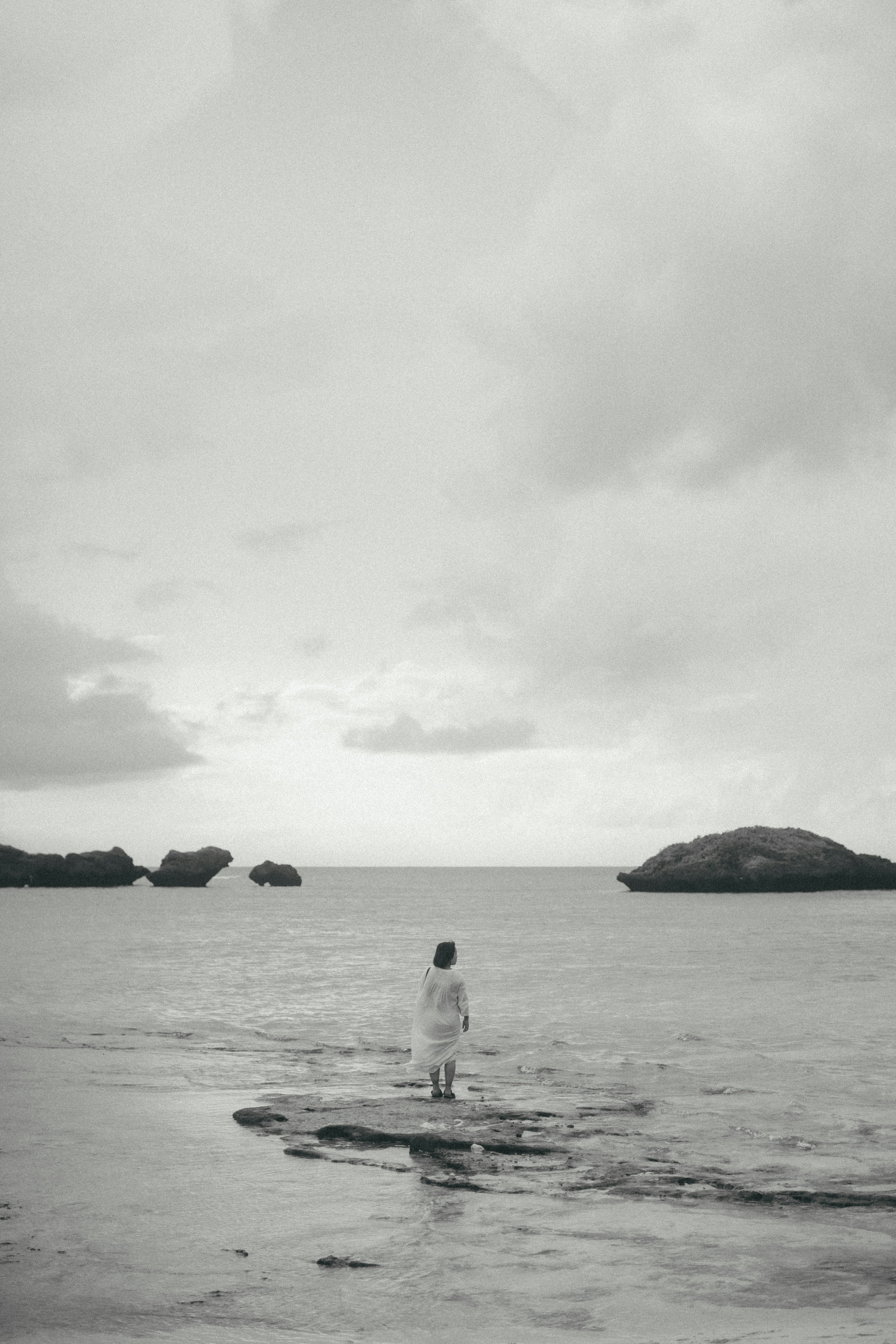 A woman in a white dress standing by the sea with a cloudy sky