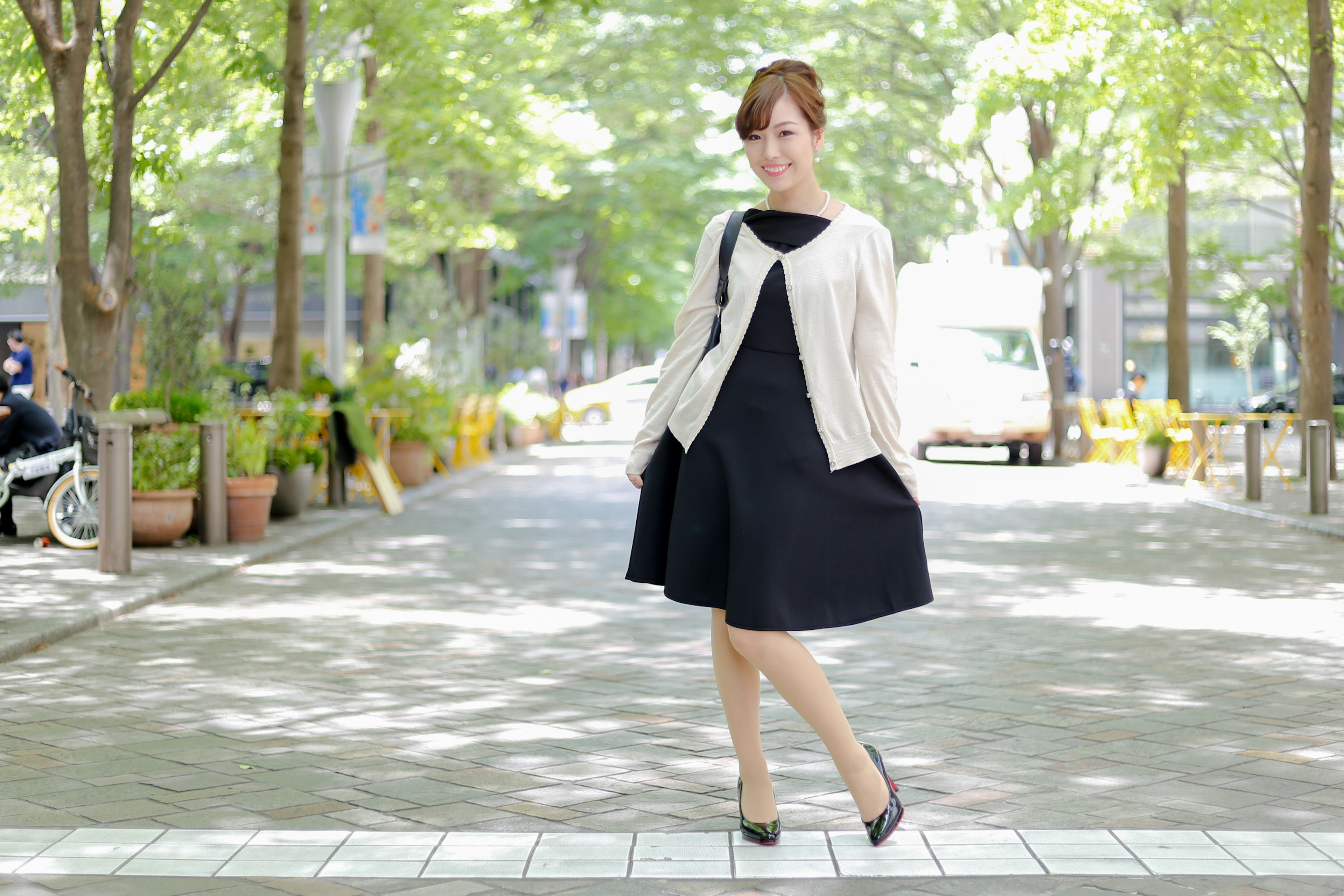 Woman in a black dress and white jacket standing in a park