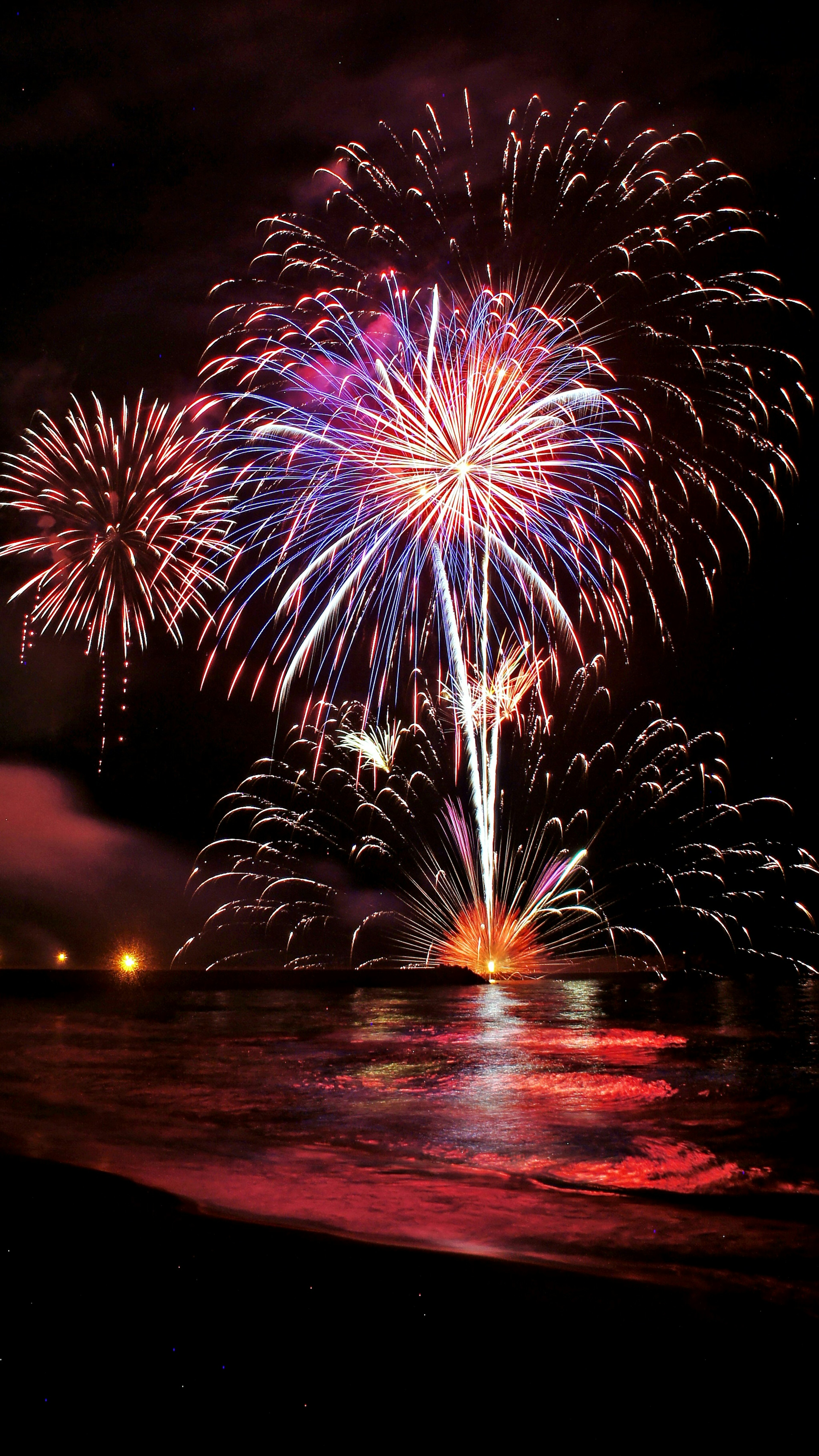 Colorful fireworks bursting in the night sky reflecting on the ocean