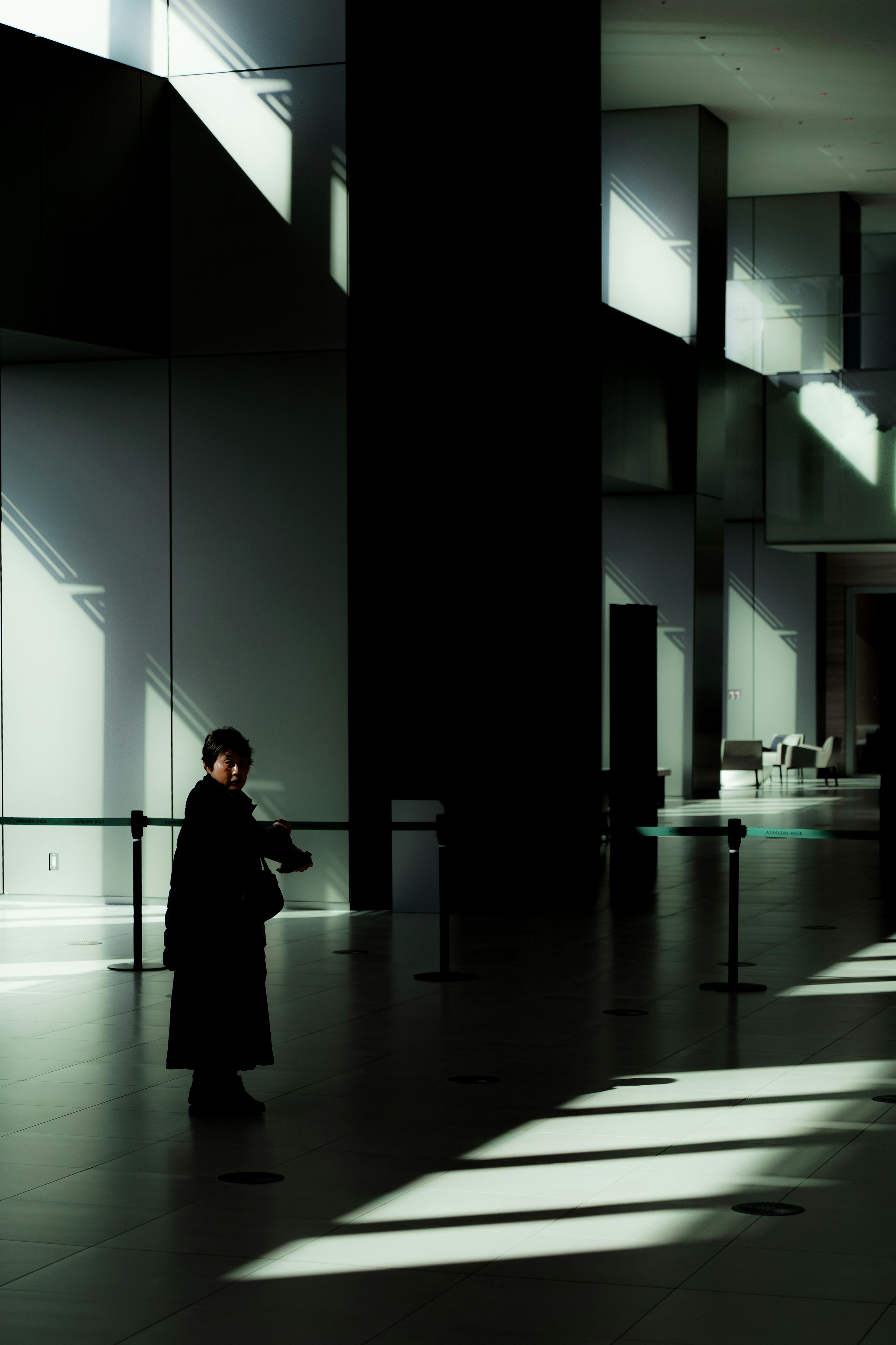 A person standing in a dark space with striking contrasts of light and shadow in a modern interior