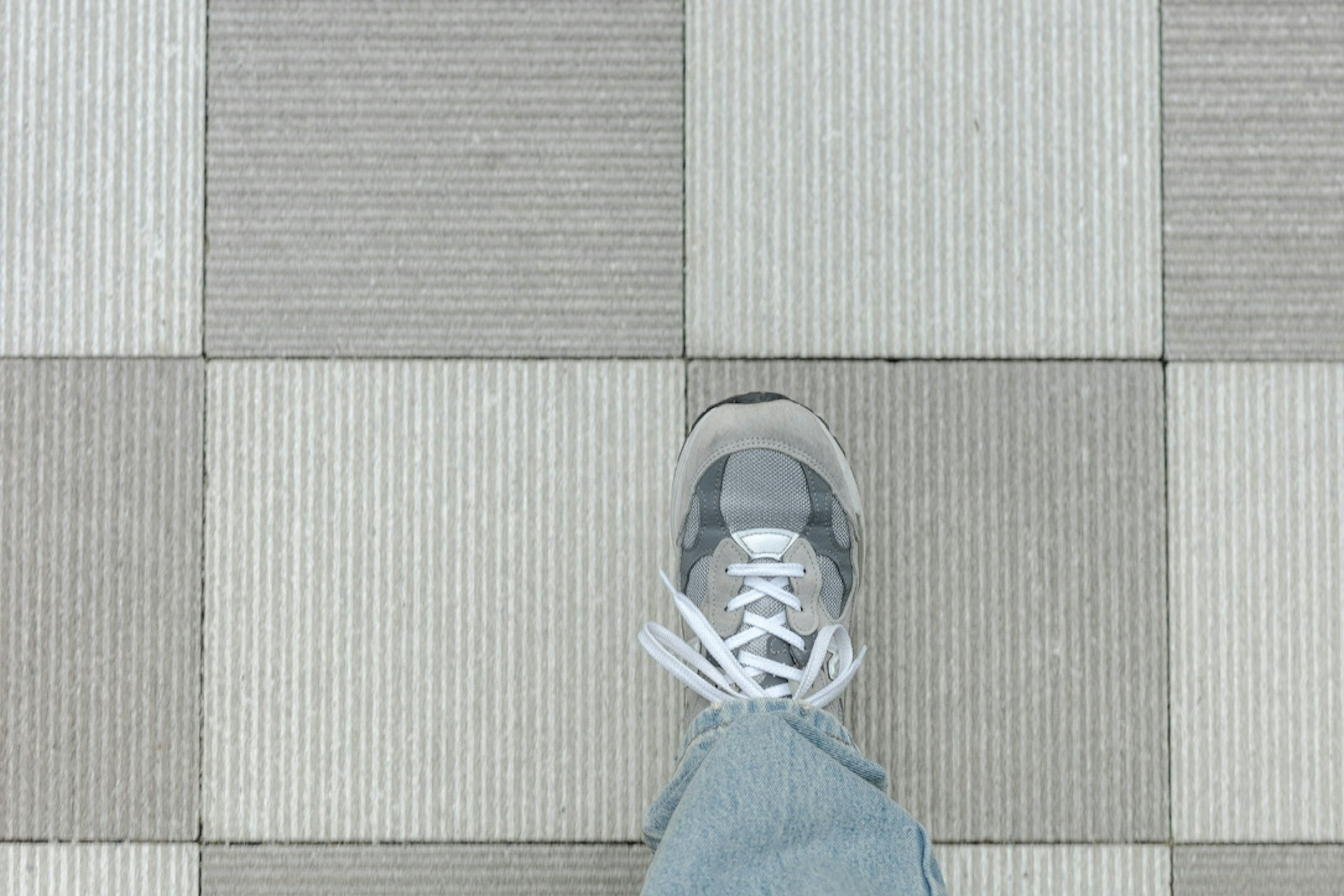 Gros plan d'une sneaker sur un sol carrelé rayé gris et blanc