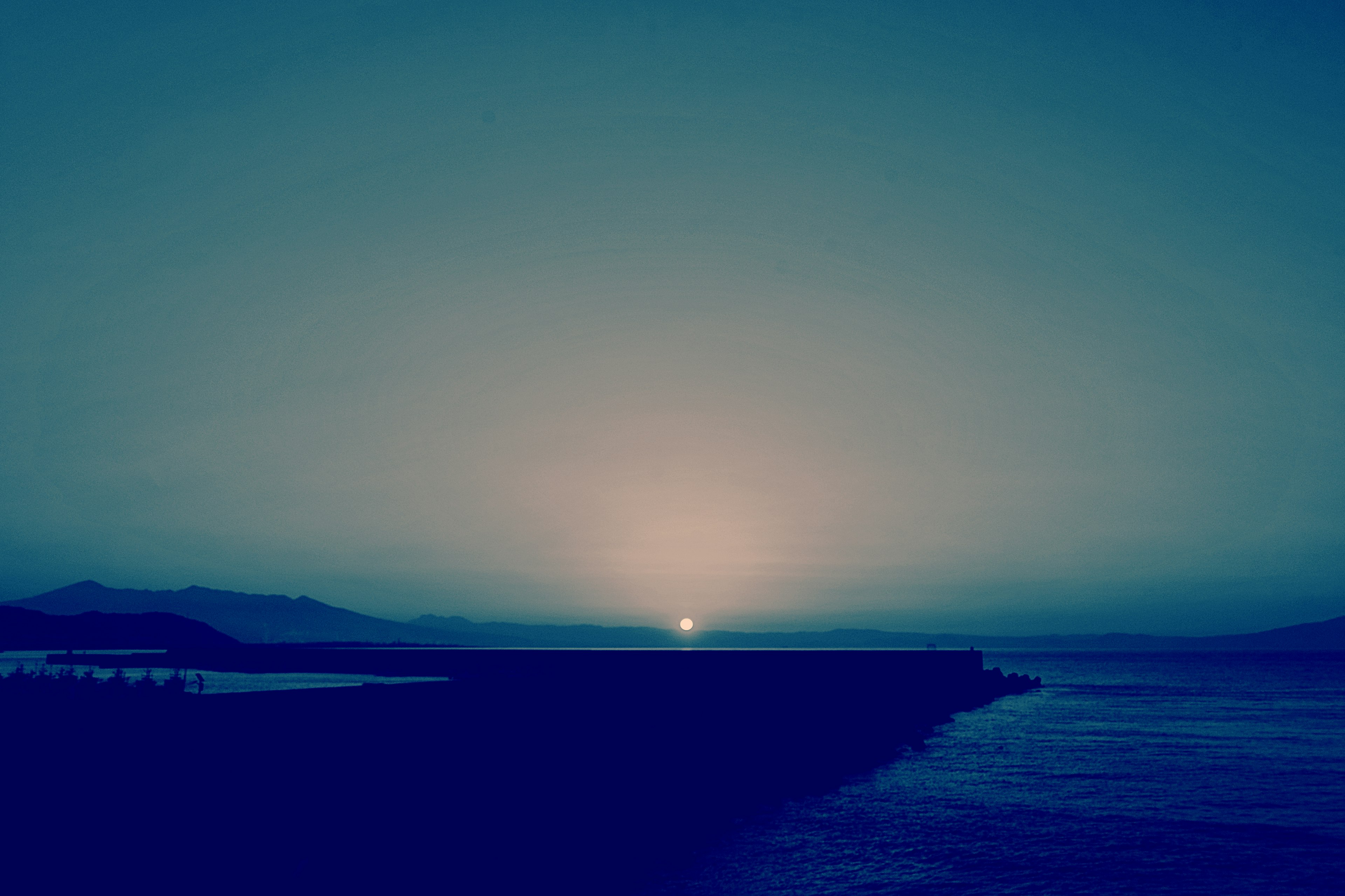 Vista oceánica en crepúsculo azul con un sol poniente a lo lejos y olas tranquilas