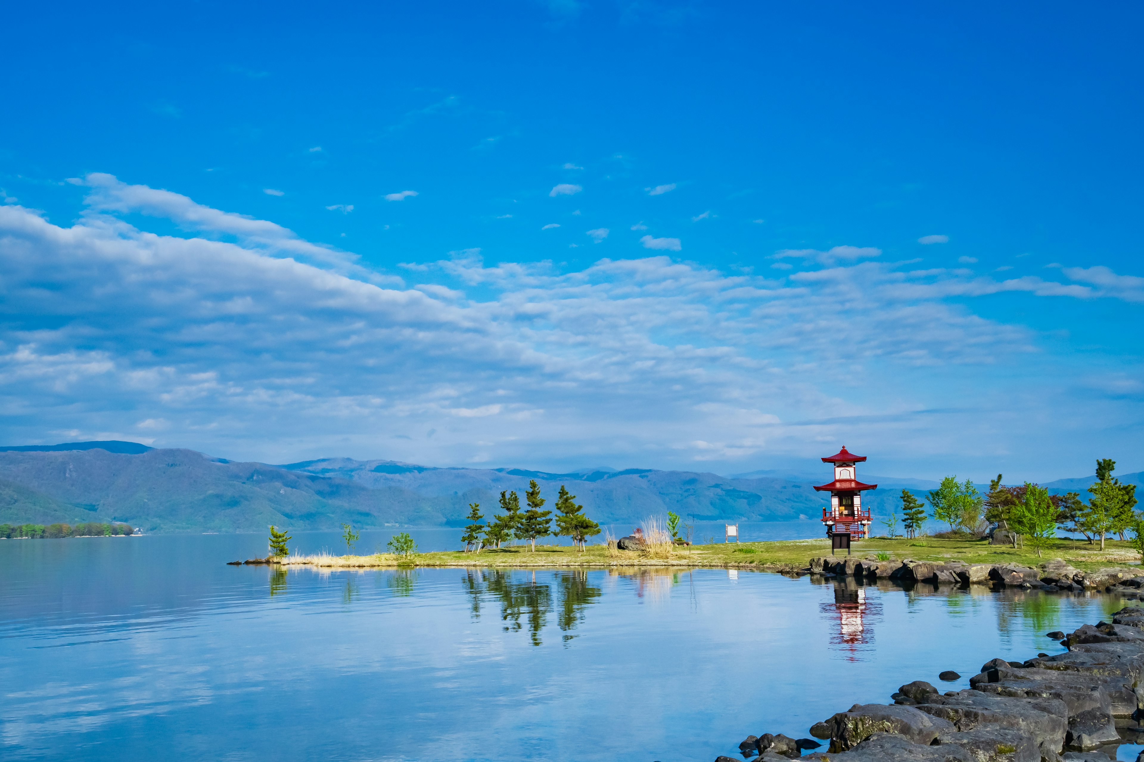 Vista panoramica di un lago tranquillo sotto un cielo blu con un faro rosso