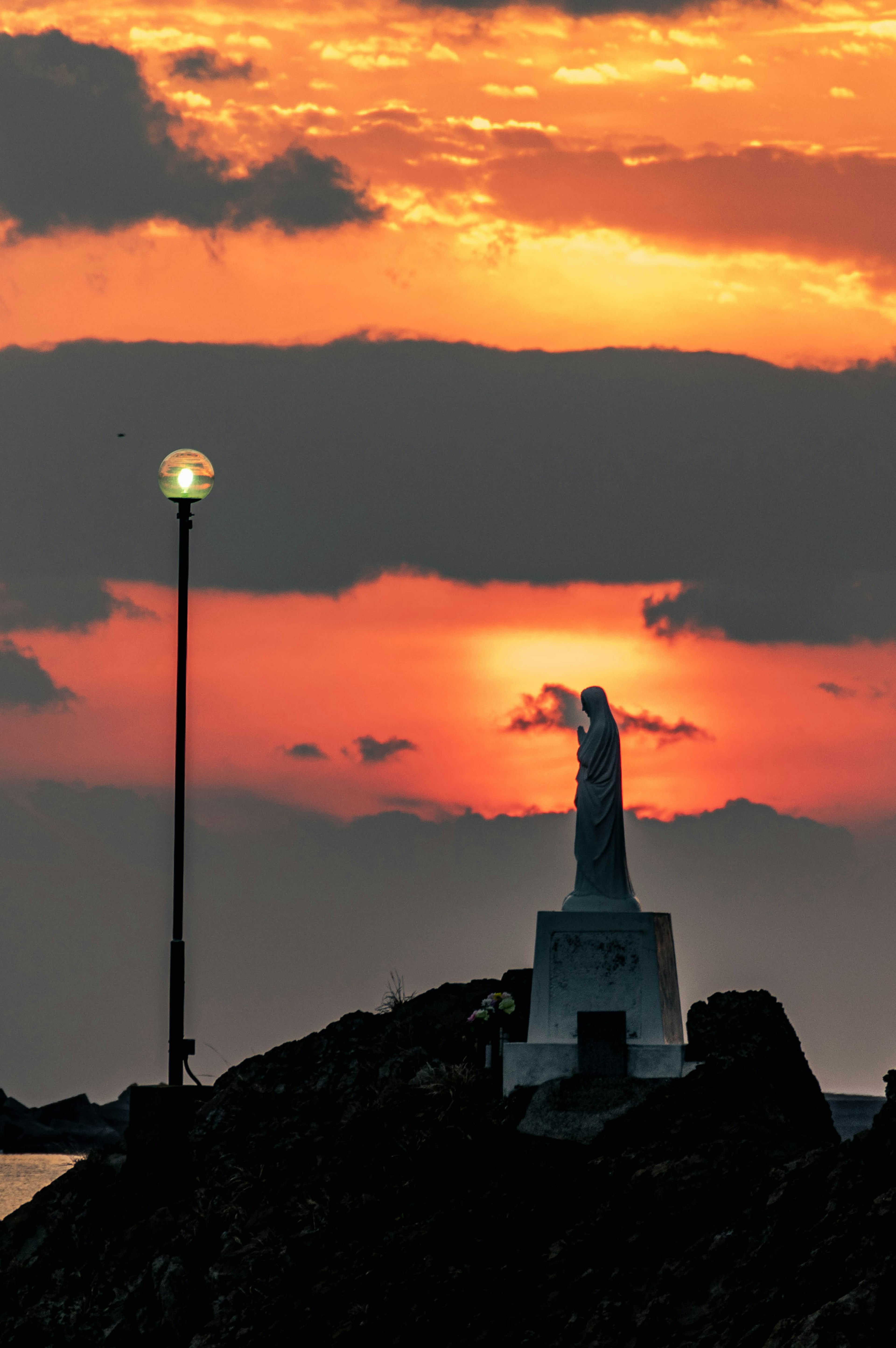 ภาพเงาของรูปปั้นและโคมไฟข้างถนนในยามพระอาทิตย์ตก