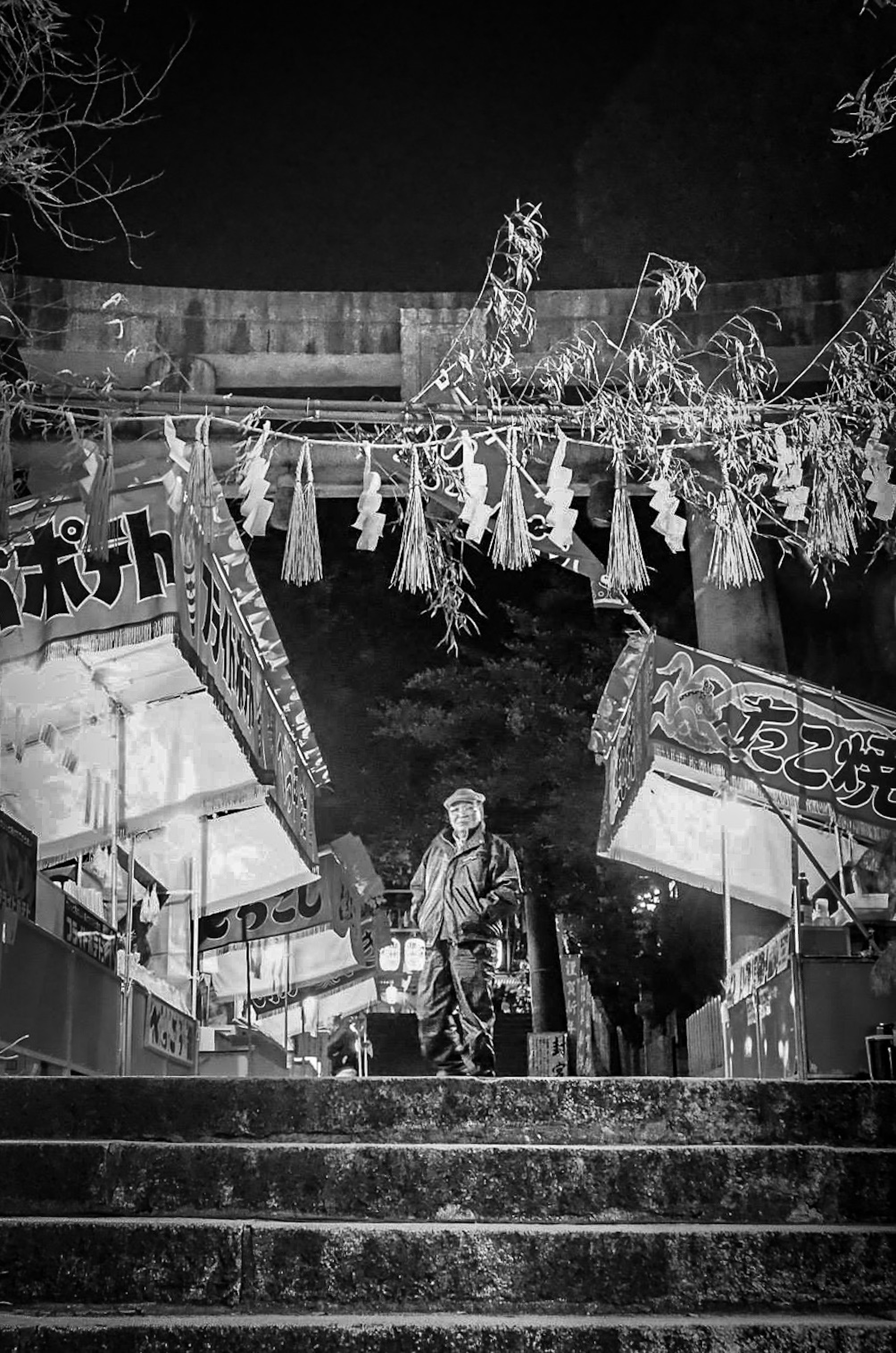 A person ascending the steps of a shrine at night with lanterns hanging from stalls