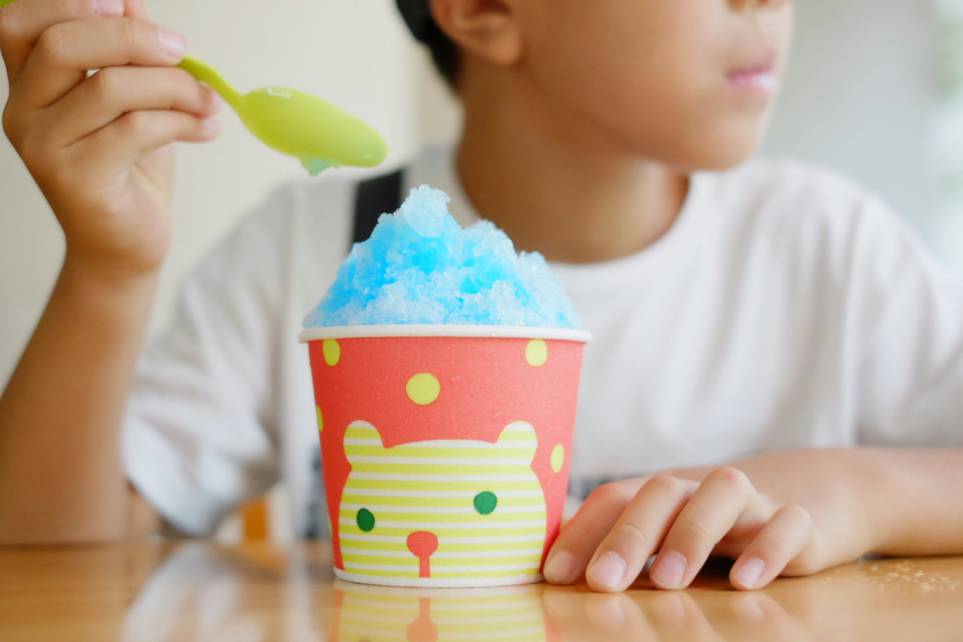 Child holding a spoon with blue shaved ice in a cute cat design cup