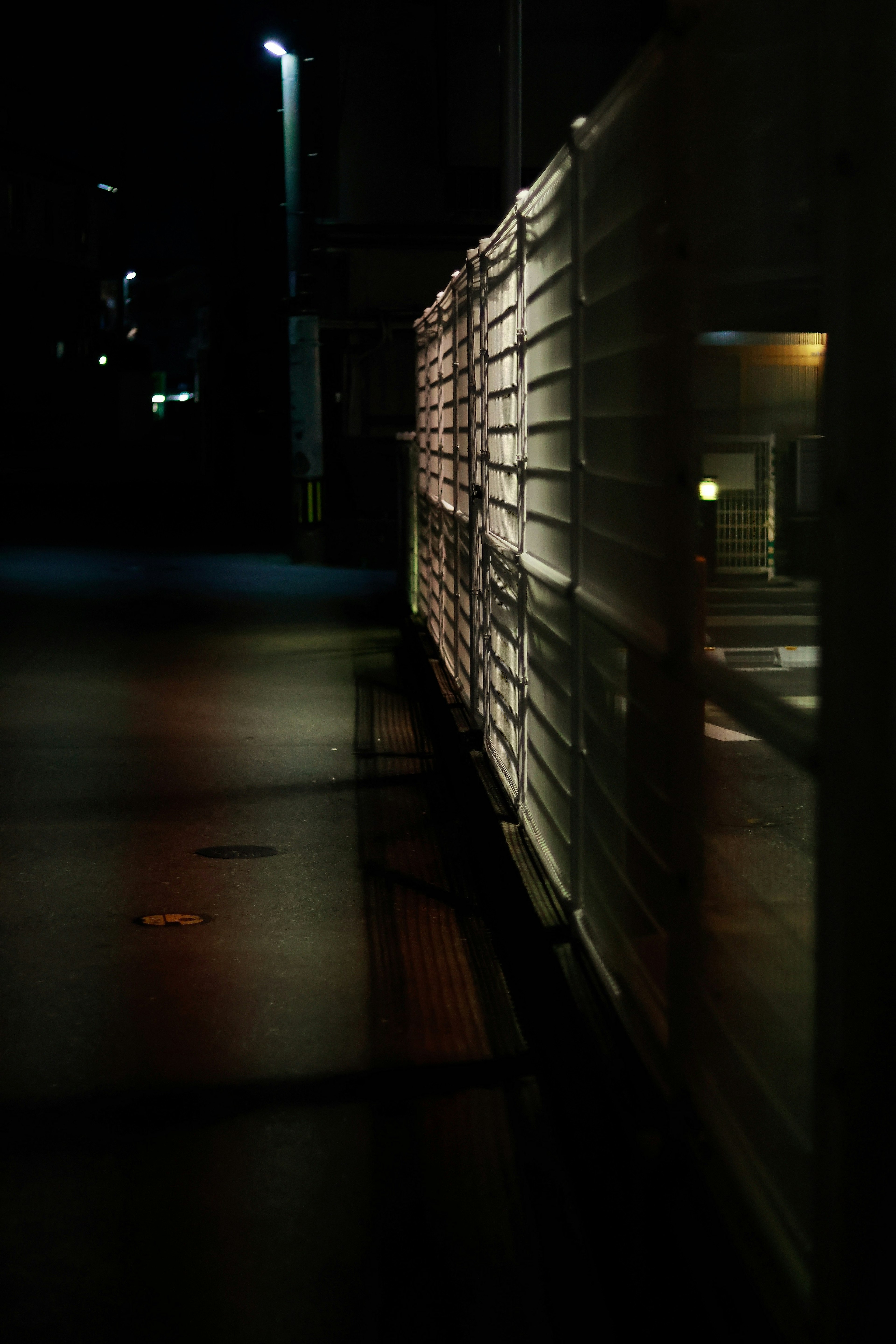 Vue latérale d'une clôture blanche le long d'une rue sombre éclairée par des lampadaires