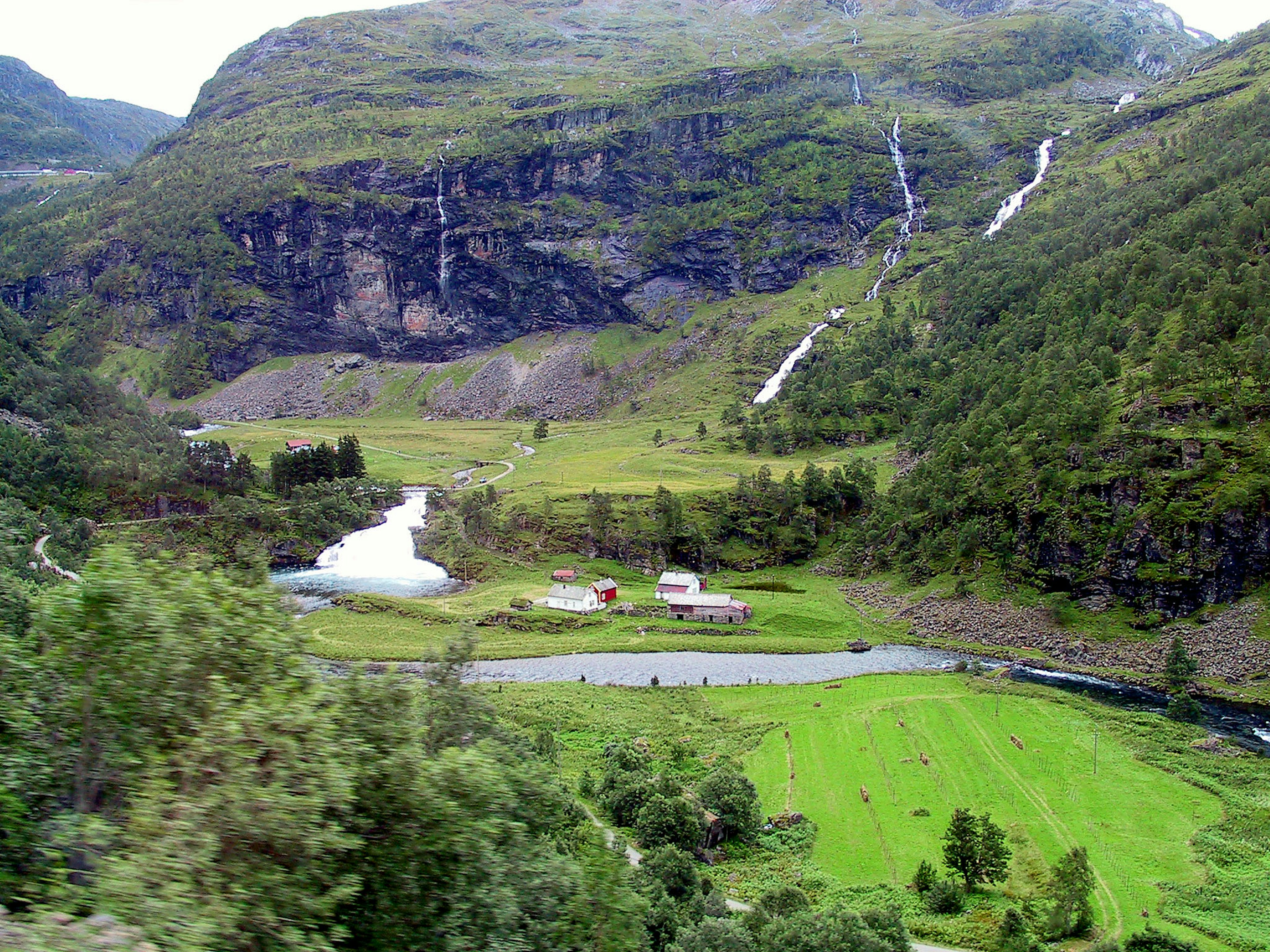 Paesaggio scenico con montagne e campi verdi un fiume che scorre e piccole fattorie sparse