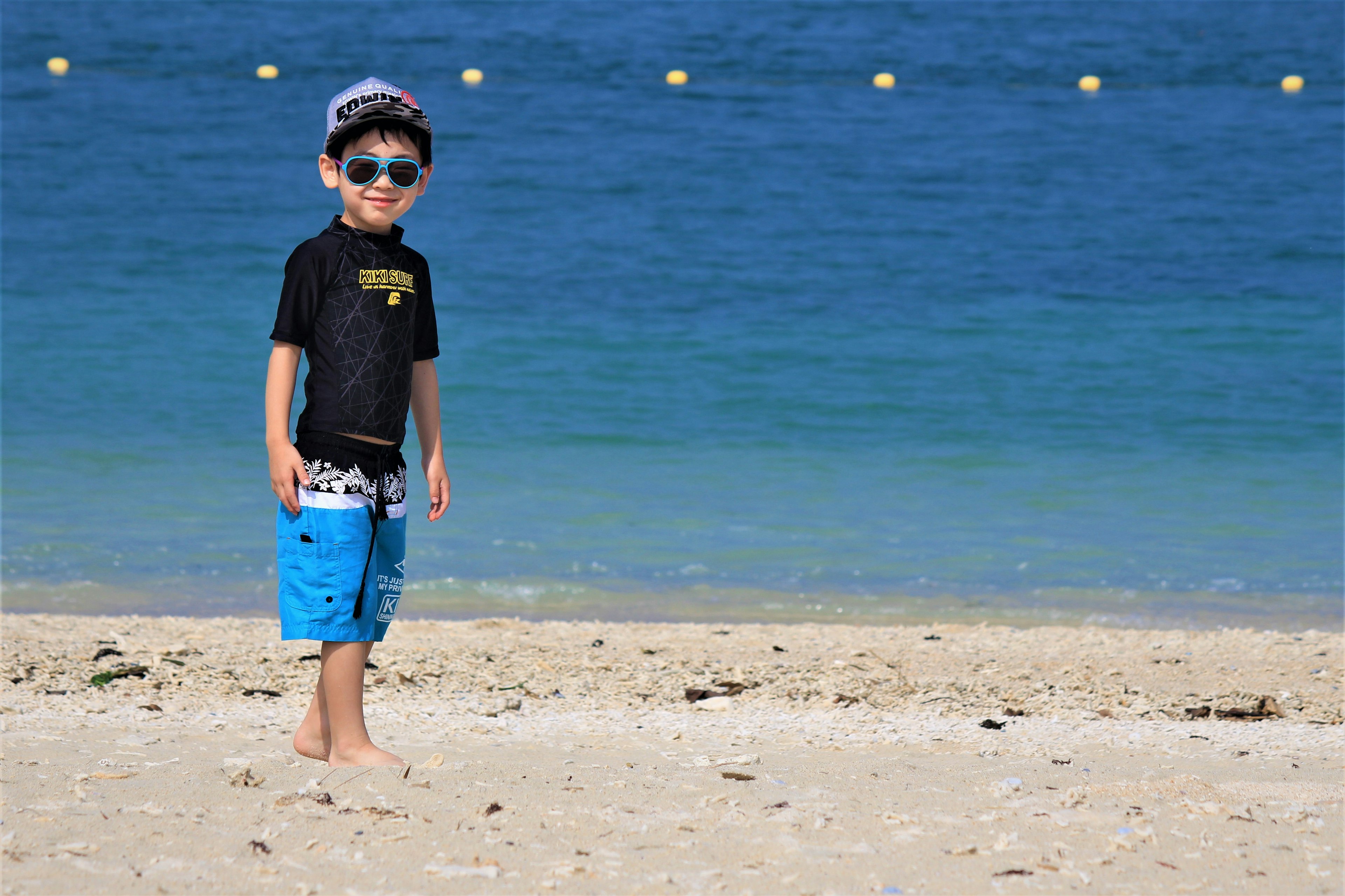 Bambino in piedi sulla spiaggia con occhiali da sole e pantaloni da bagno