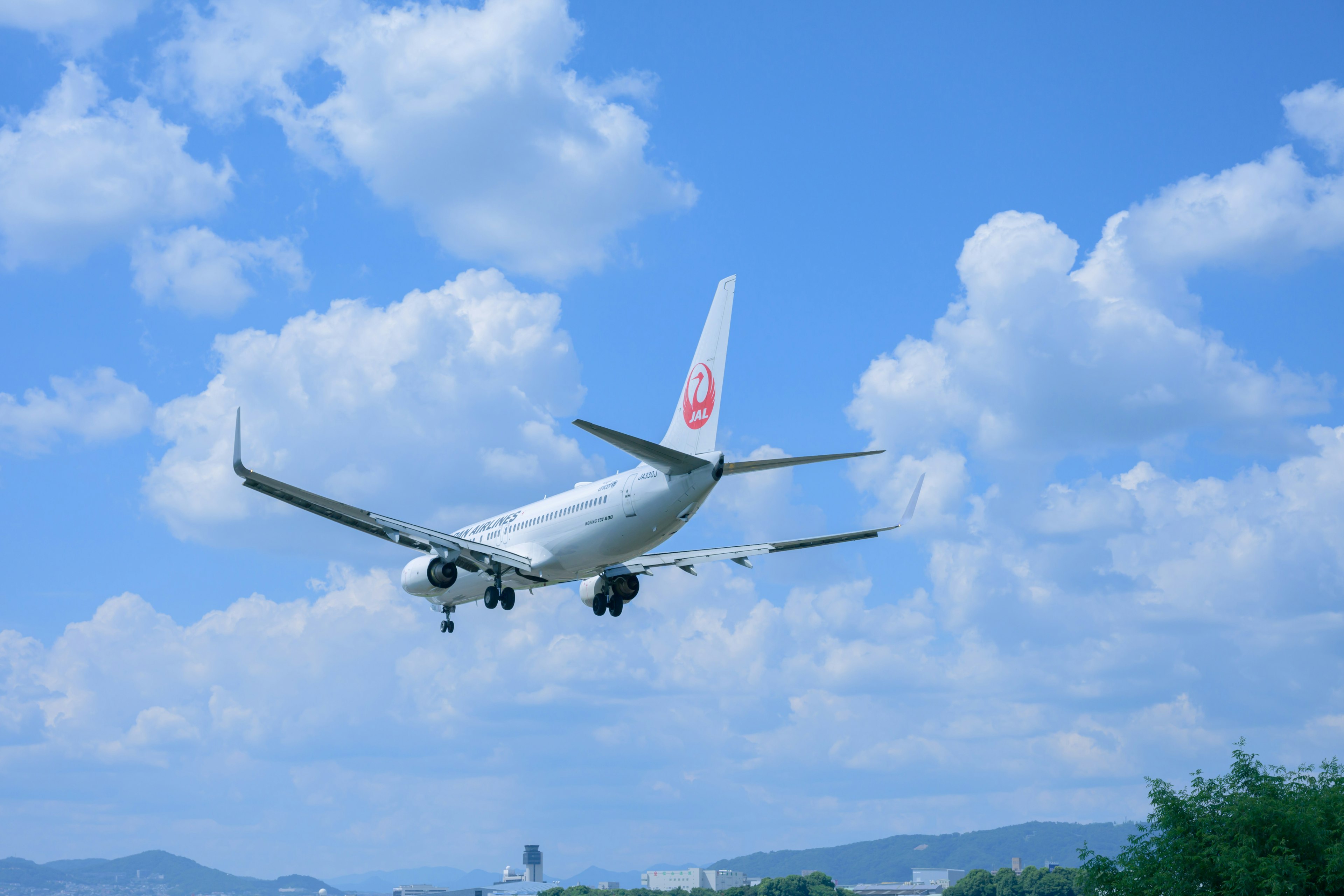 A white airplane landing under a blue sky with fluffy white clouds