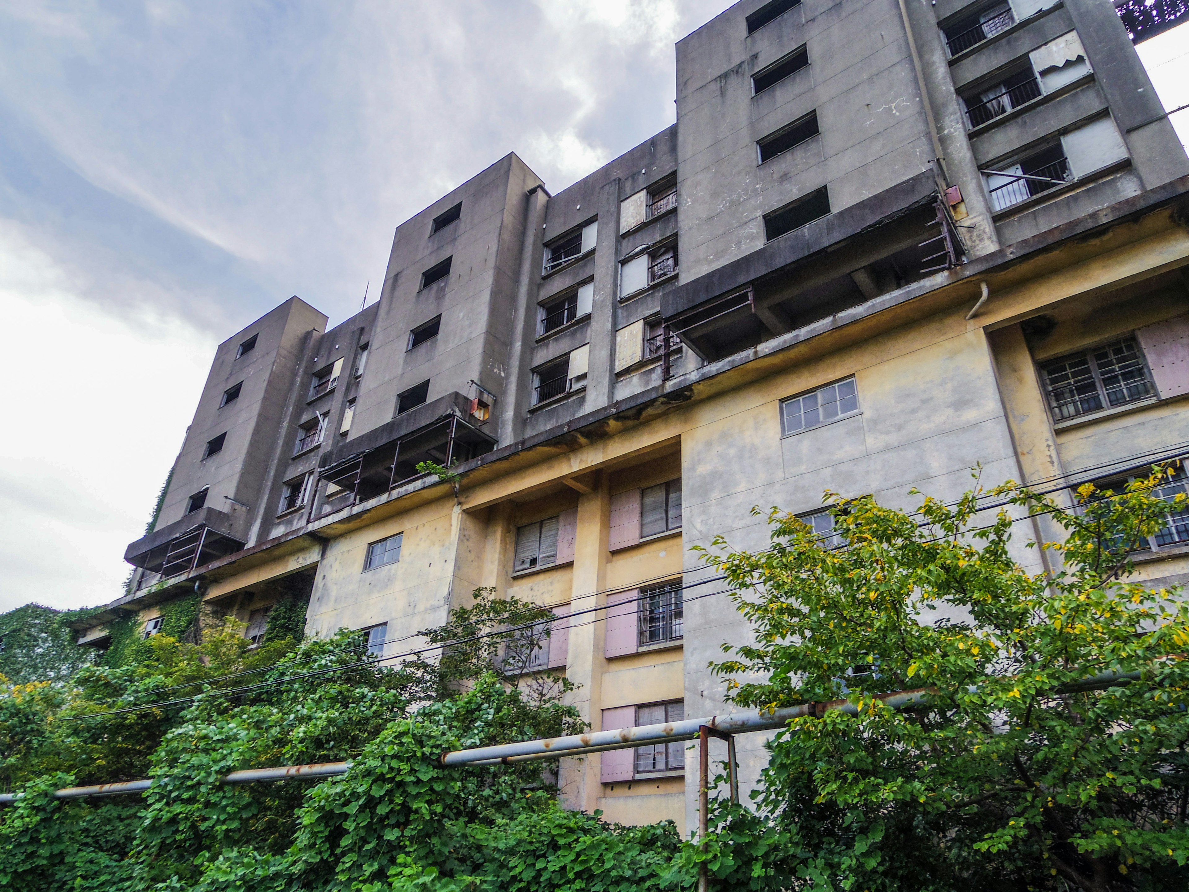 Exterior view of an abandoned apartment building surrounded by lush greenery