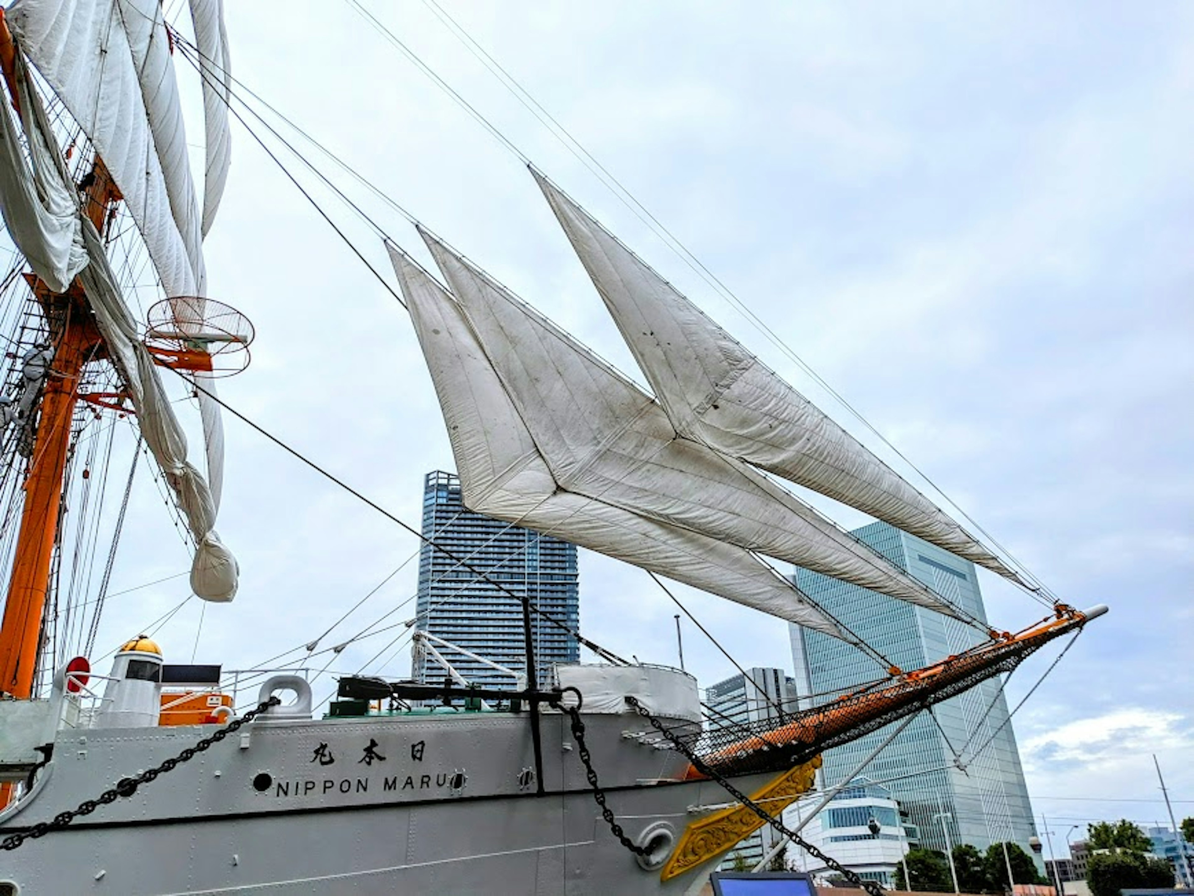 Sailing ship with white sails and modern buildings in the background