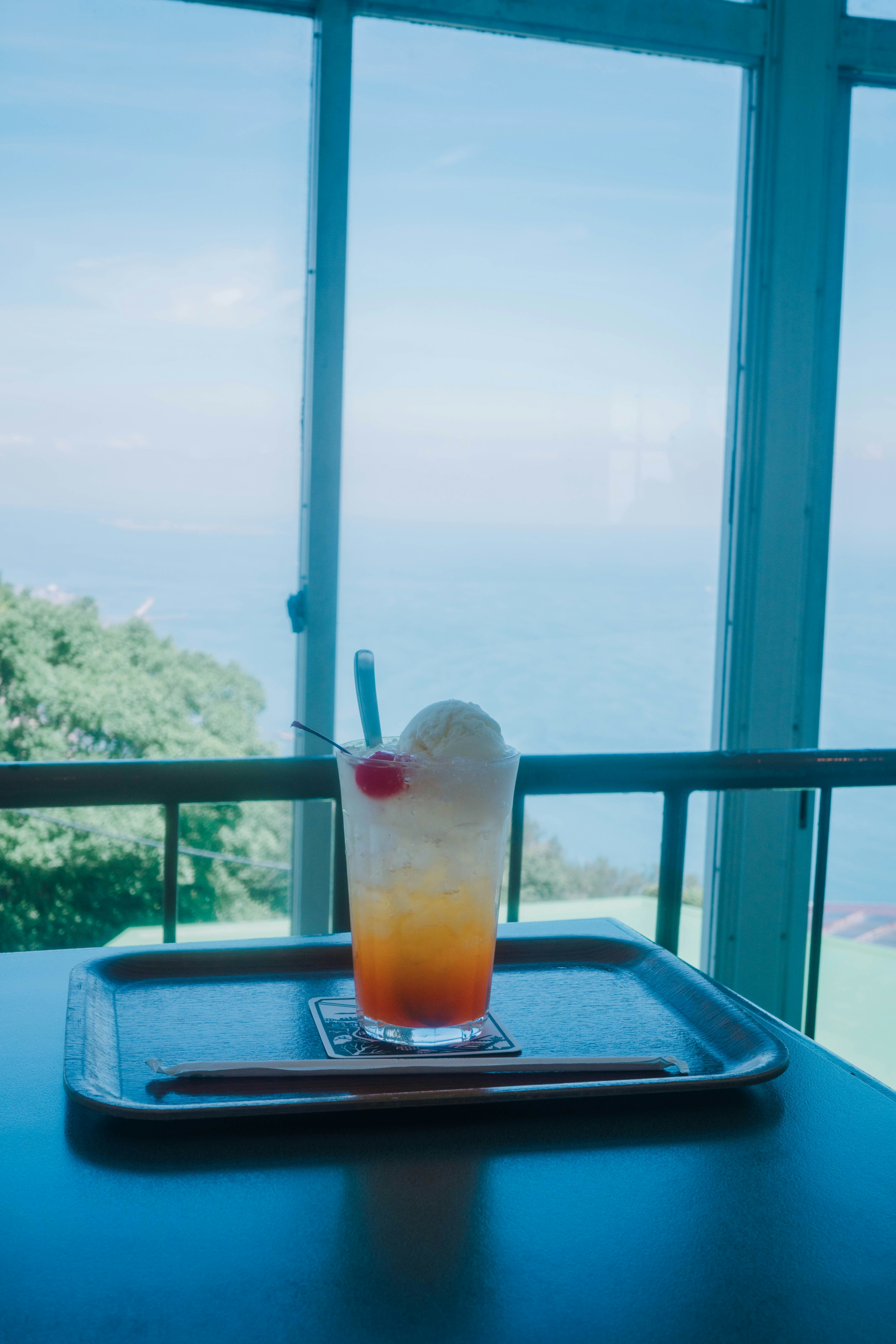 Calice di cocktail con ciliegia su un vassoio vicino a una finestra che si affaccia sul mare