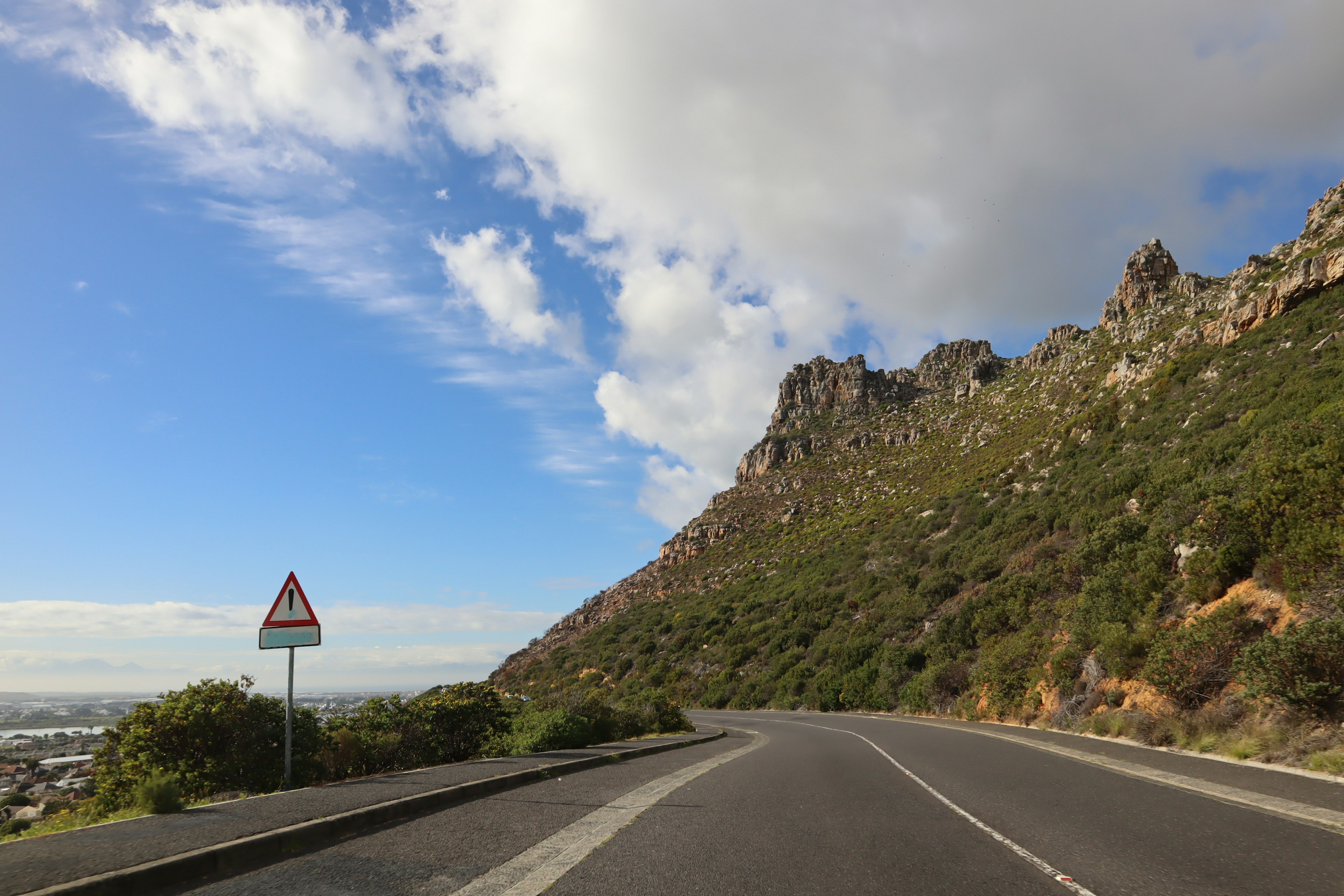 Route courbée le long d'une montagne sous un ciel bleu et des nuages