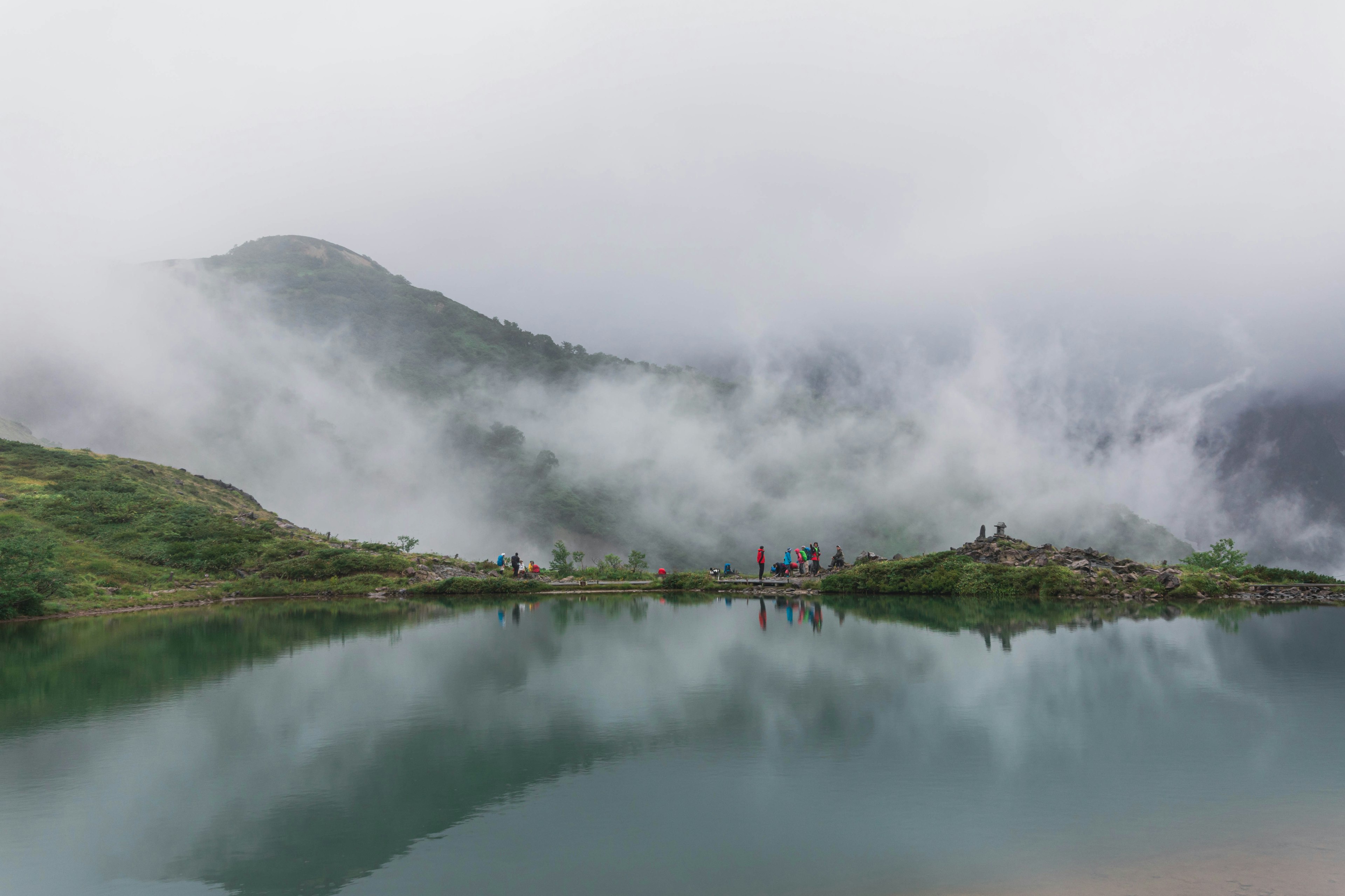 Pemandangan gunung berkabut dengan danau tenang orang-orang terlihat di kejauhan