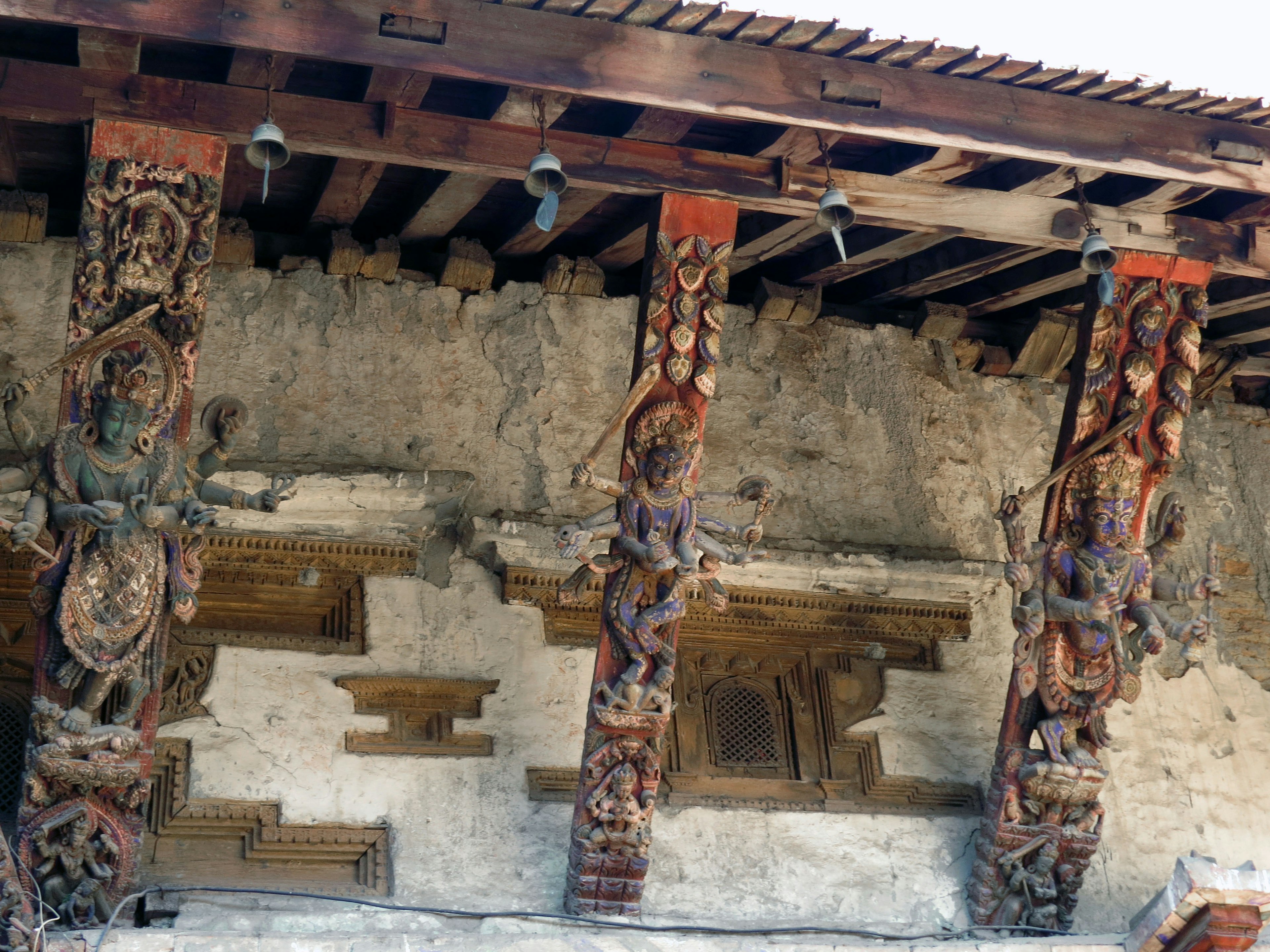 Intricate carved pillars beneath a wooden roof with ancient wall remnants