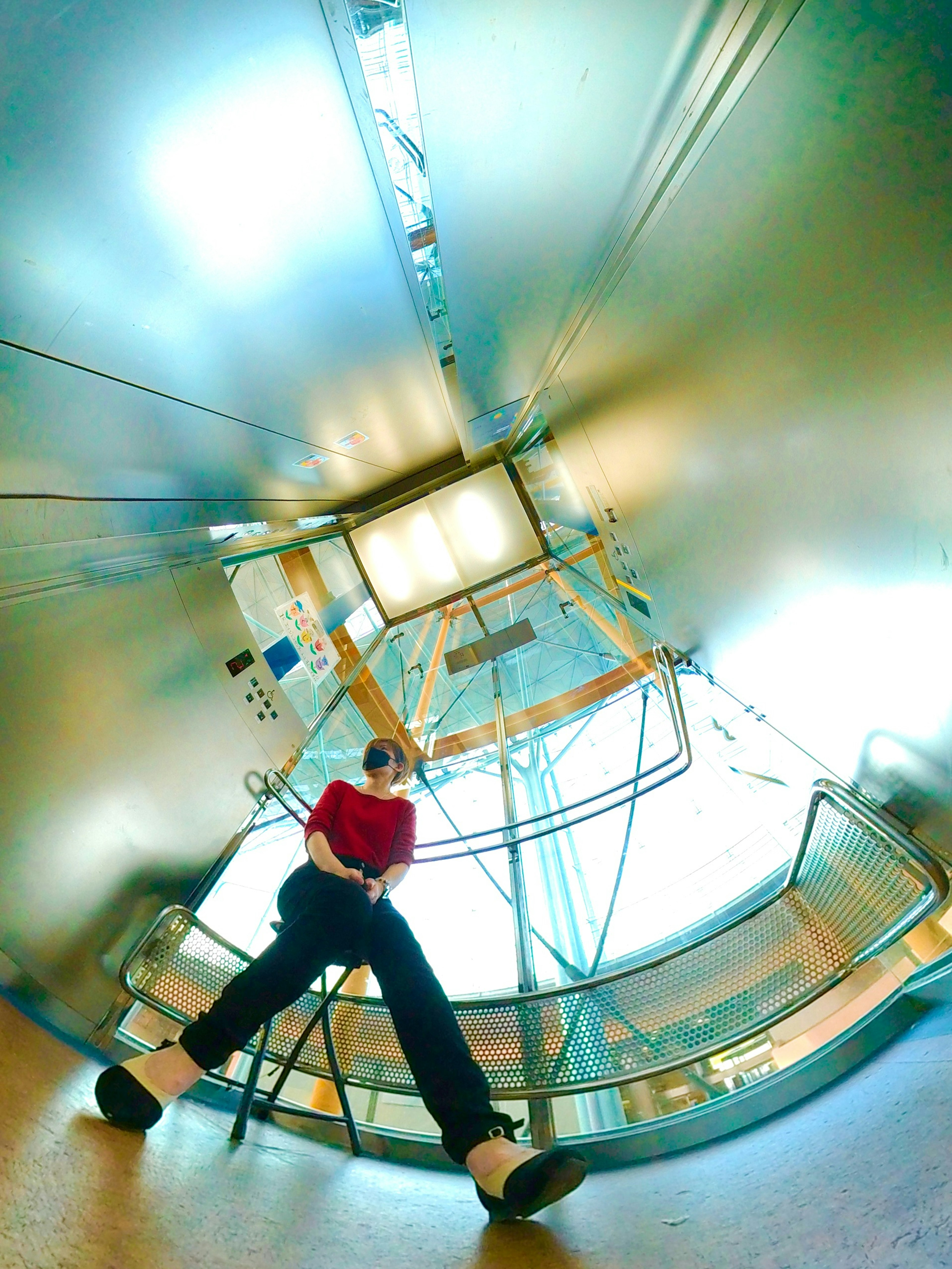 Person wearing a red shirt sitting on a stool in a metallic space