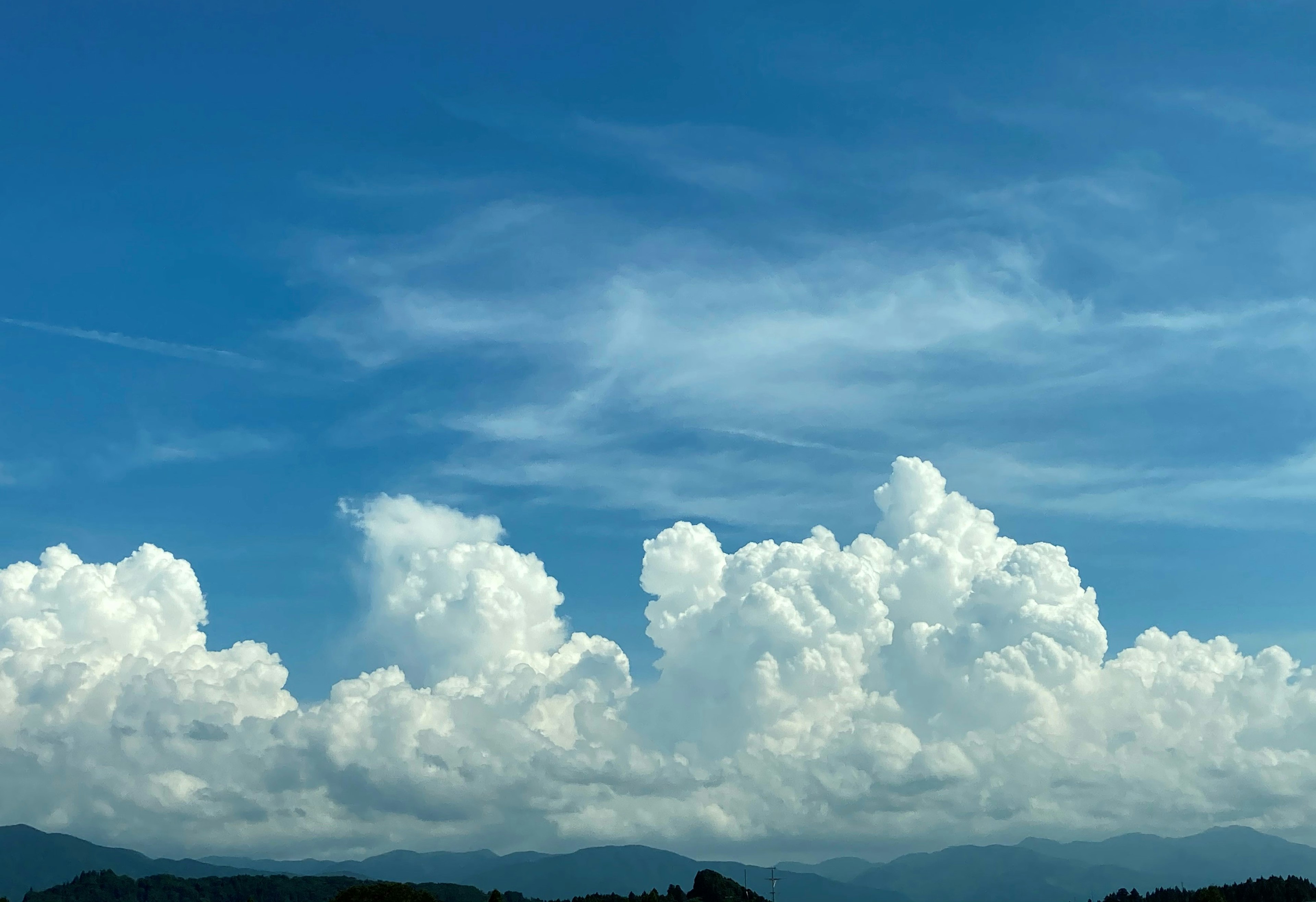 Weiße Wolken, die in einem blauen Himmel mit entfernten Bergen schweben