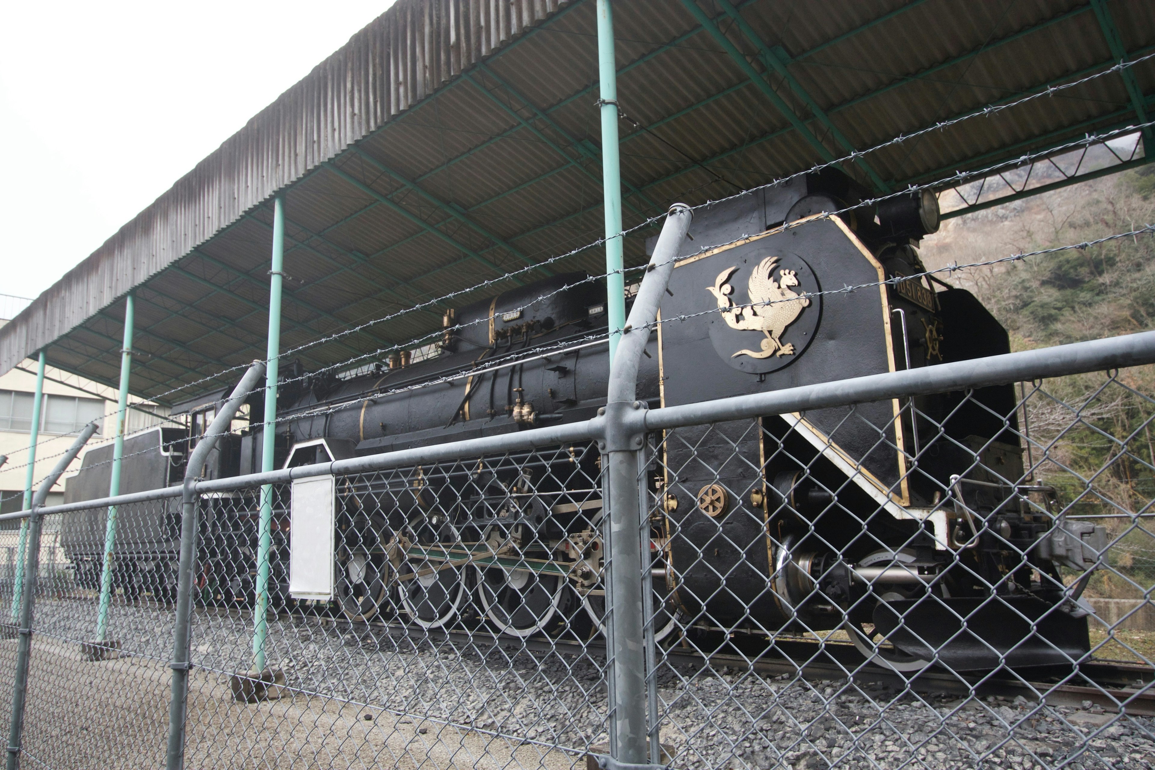 A black steam locomotive displayed under a roof with a fence surrounding it