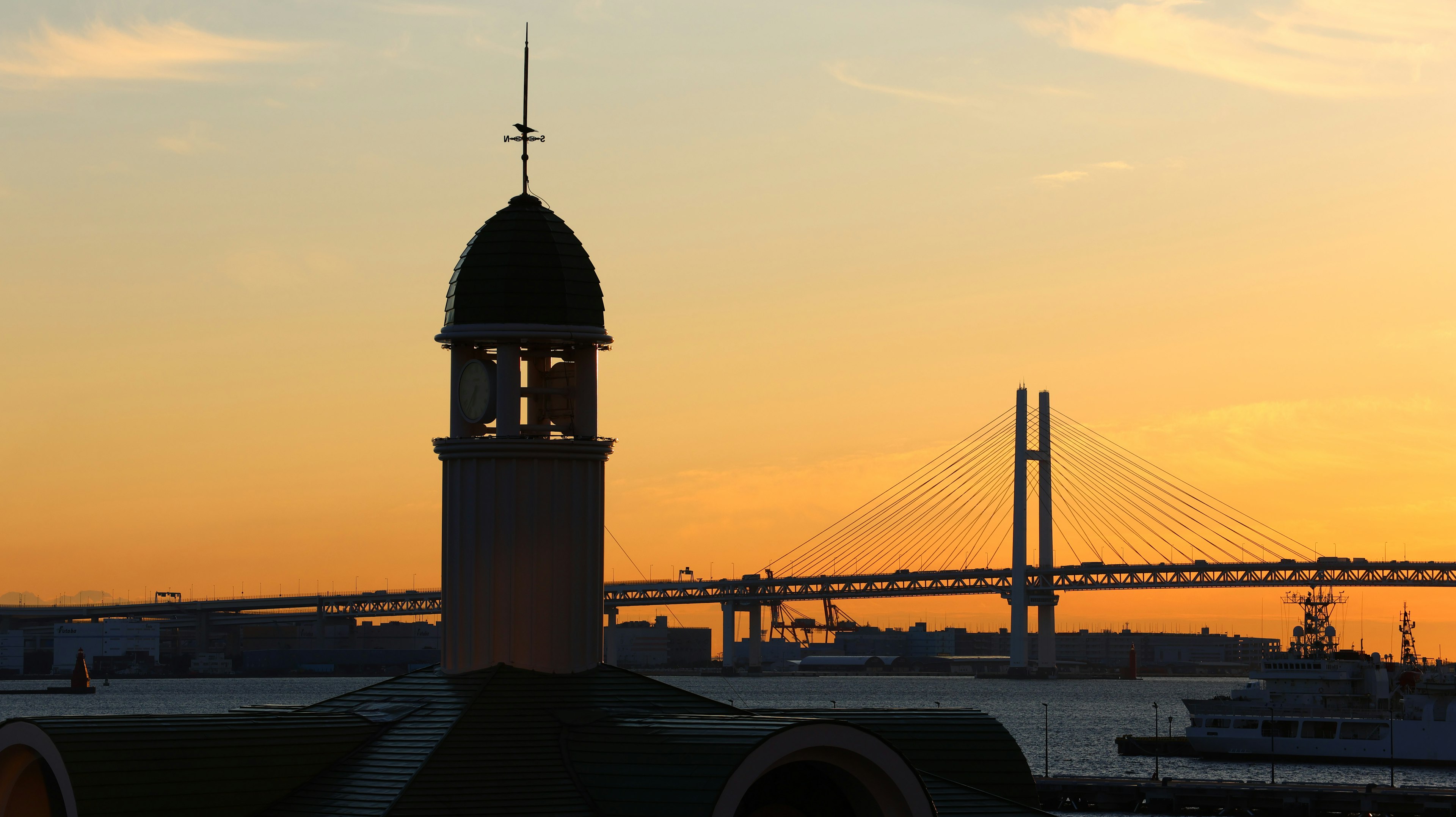 Torre in silhouette contro un tramonto con il ponte della baia a Yokohama