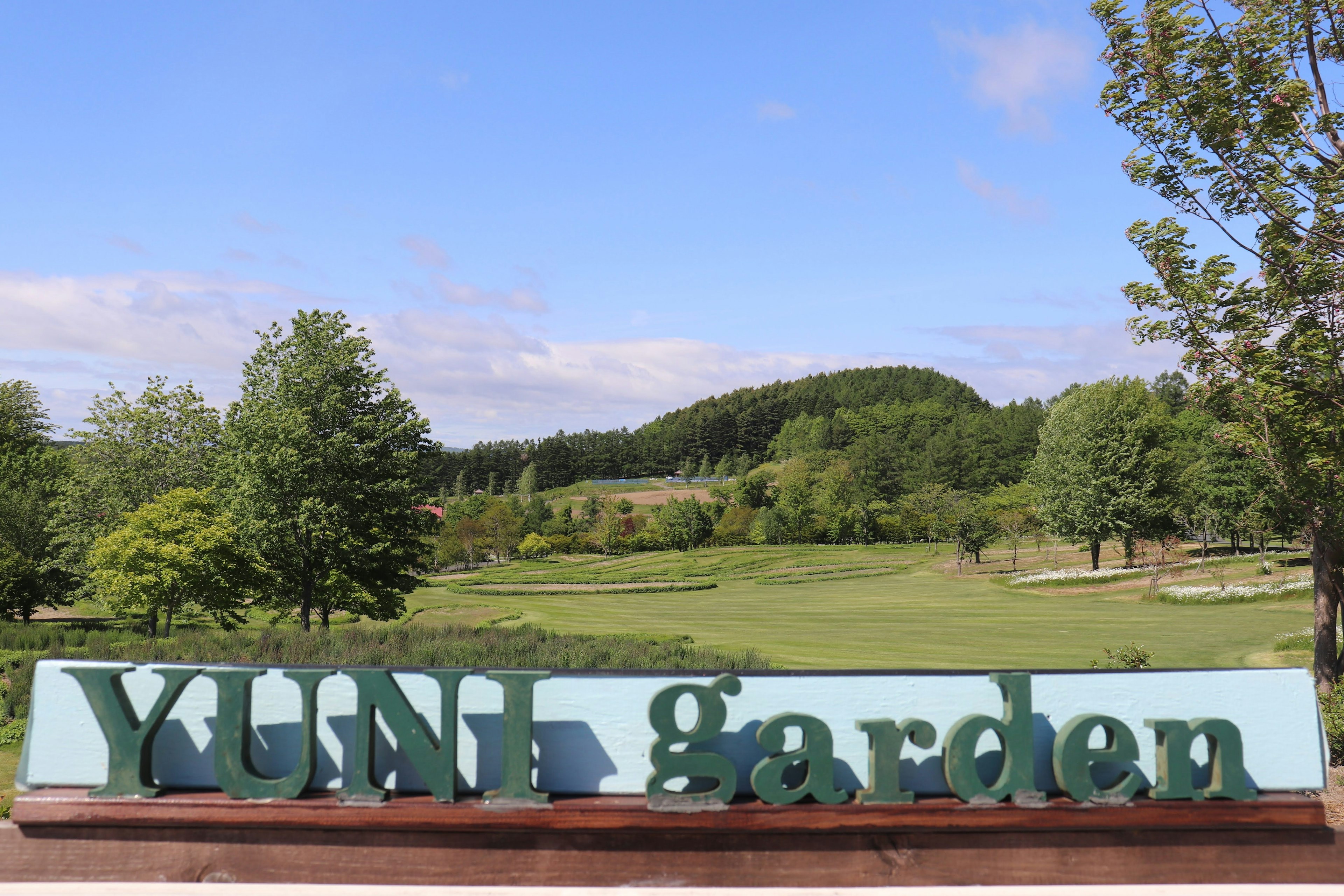 Schild des YUNI Gartens mit üppiger grüner Landschaft