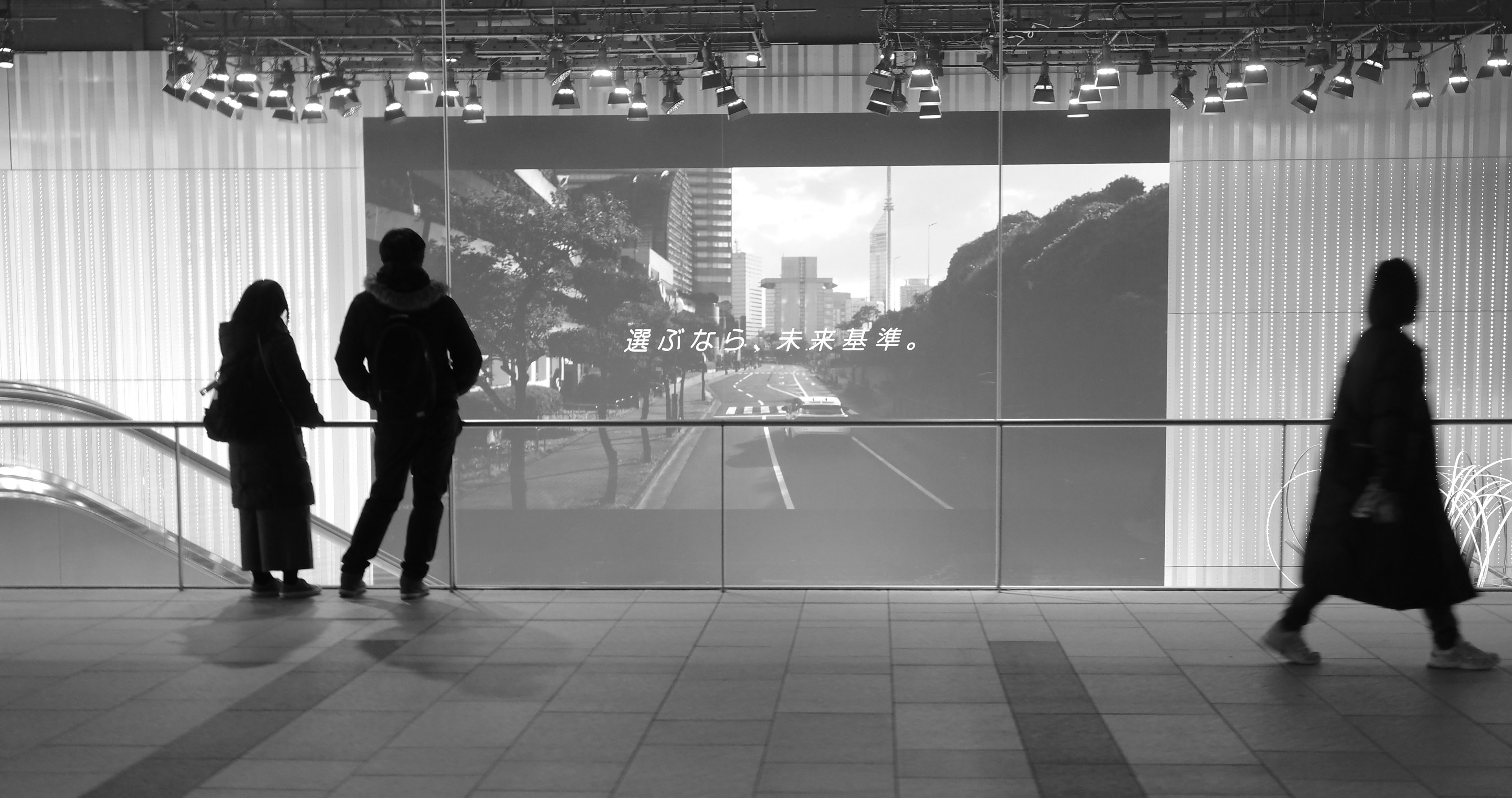 Deux observateurs et un passant devant un paysage urbain en noir et blanc